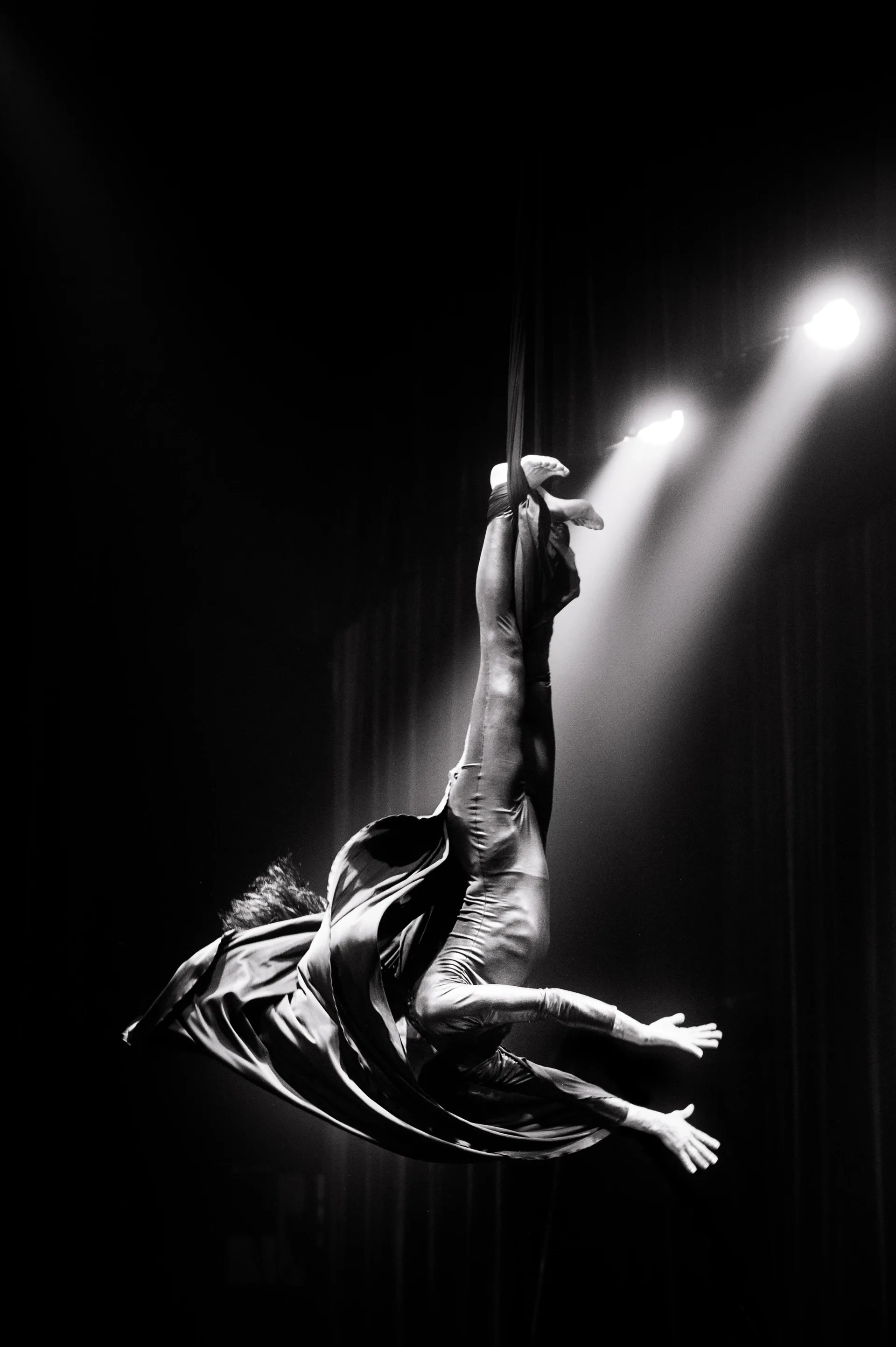 Aerial performer extends horizontally from one arm with a flowing costume.