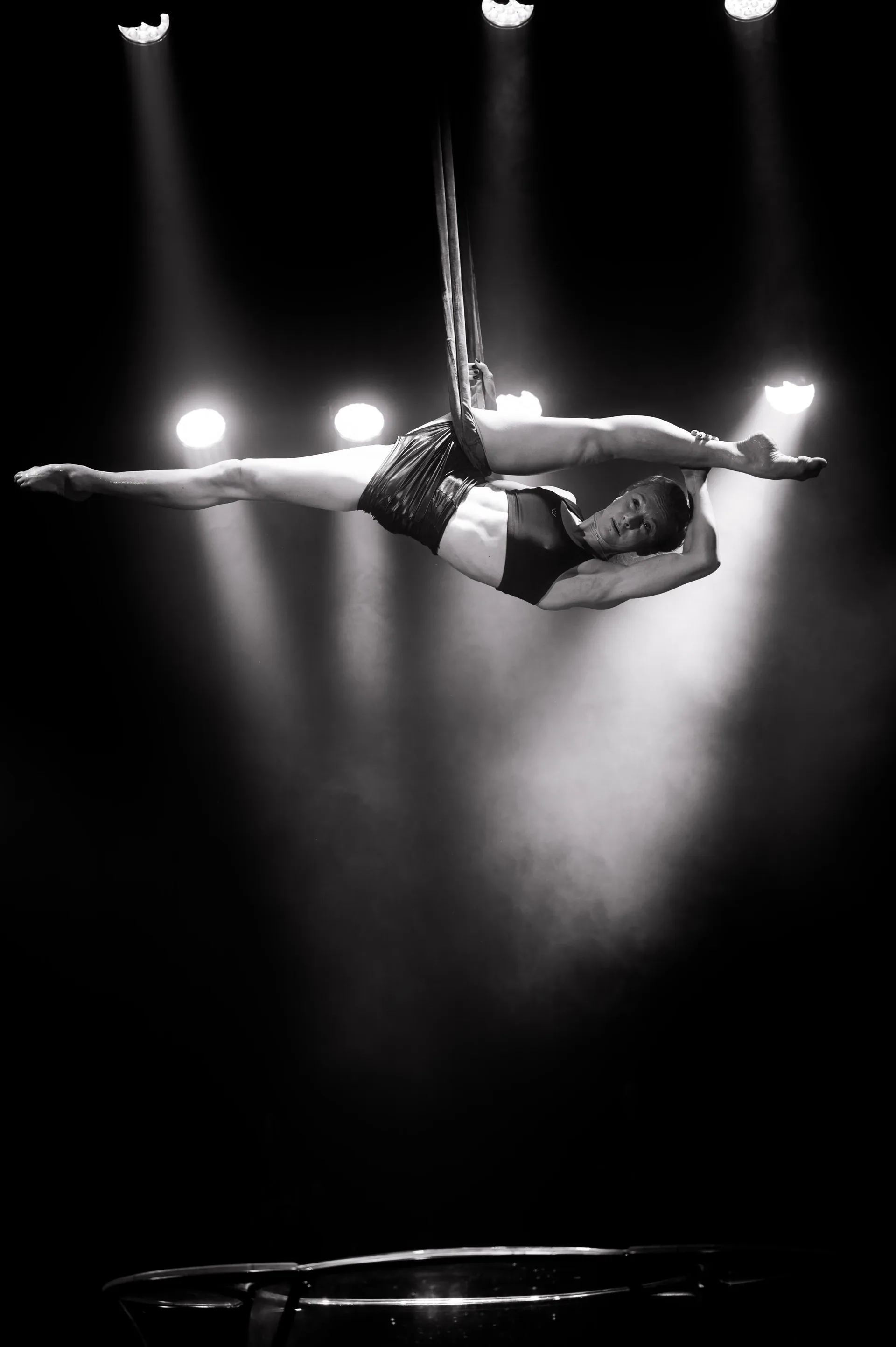 Aerial performer holds a horizontal pose while suspended from straps.