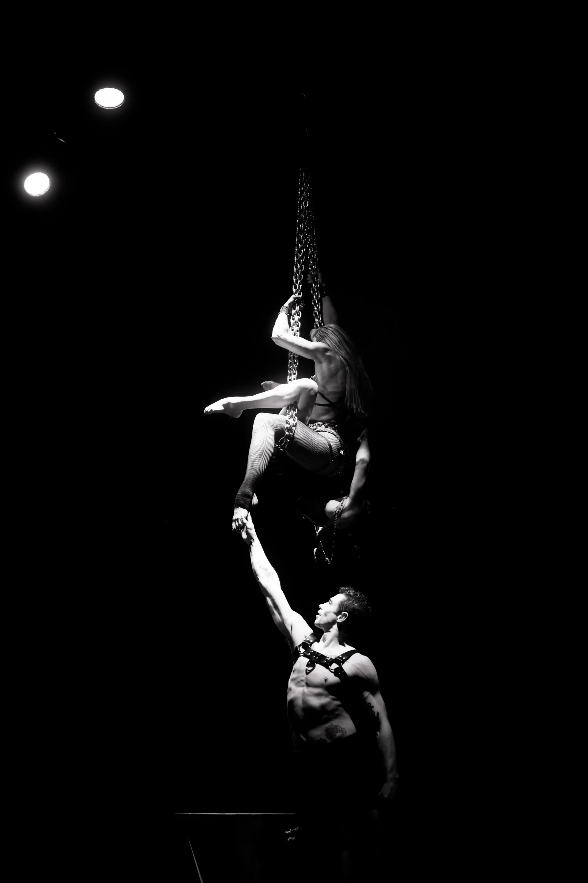 Aerial performer arches around a vertical strap above another performer.