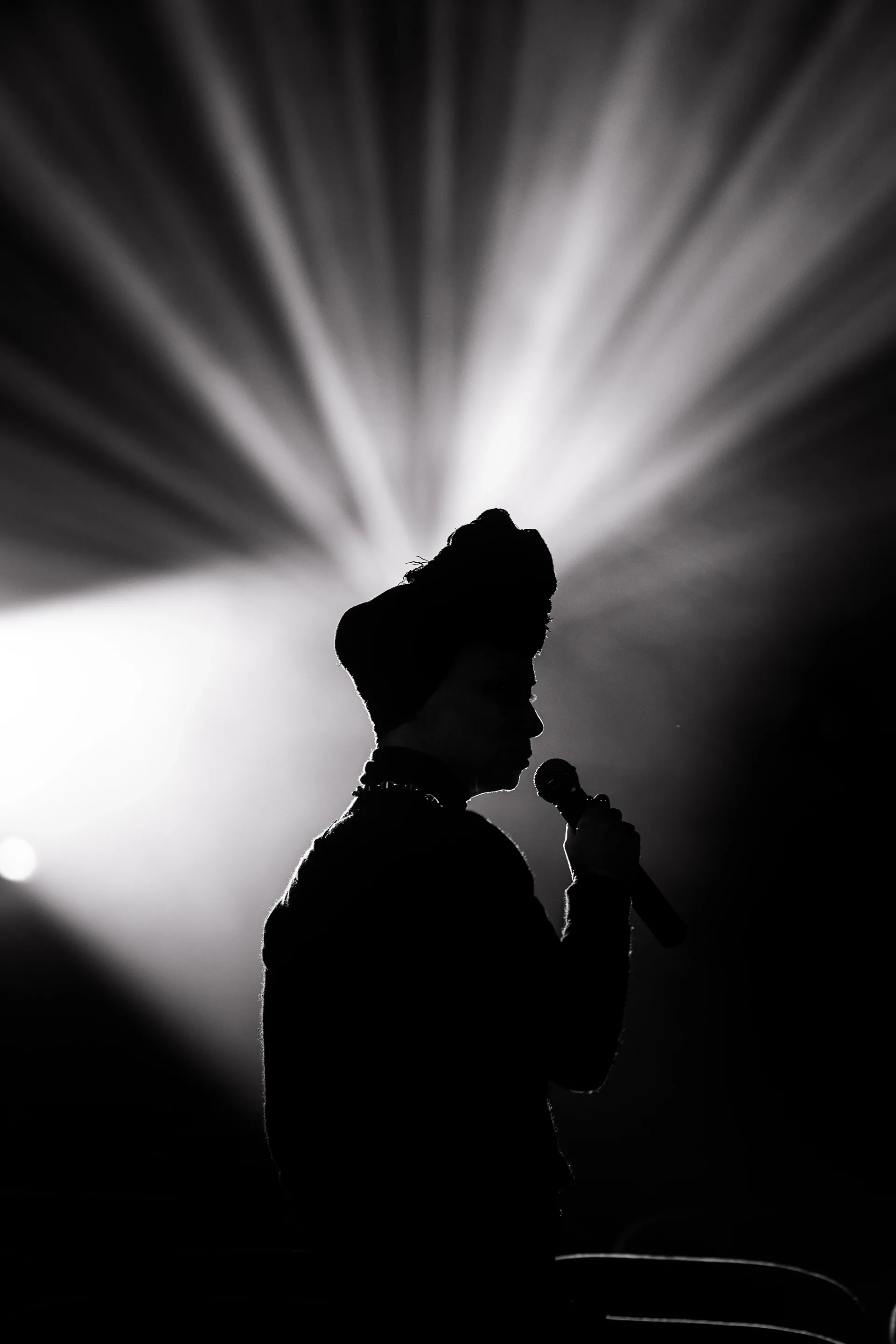 Silhouetted performer holds a microphone in front of radiating stage light.