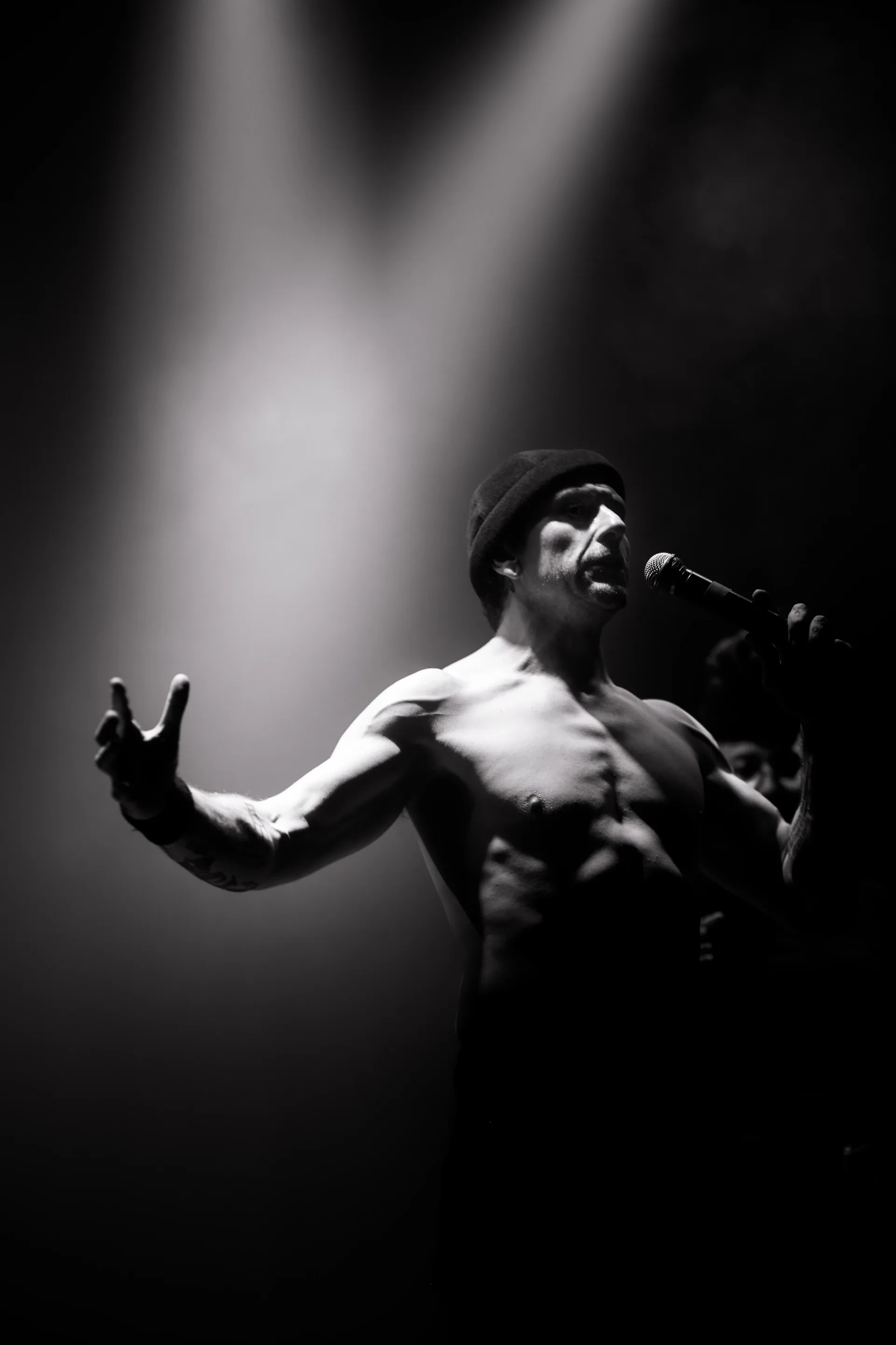 Performer sings into a handheld microphone beneath a spotlight.
