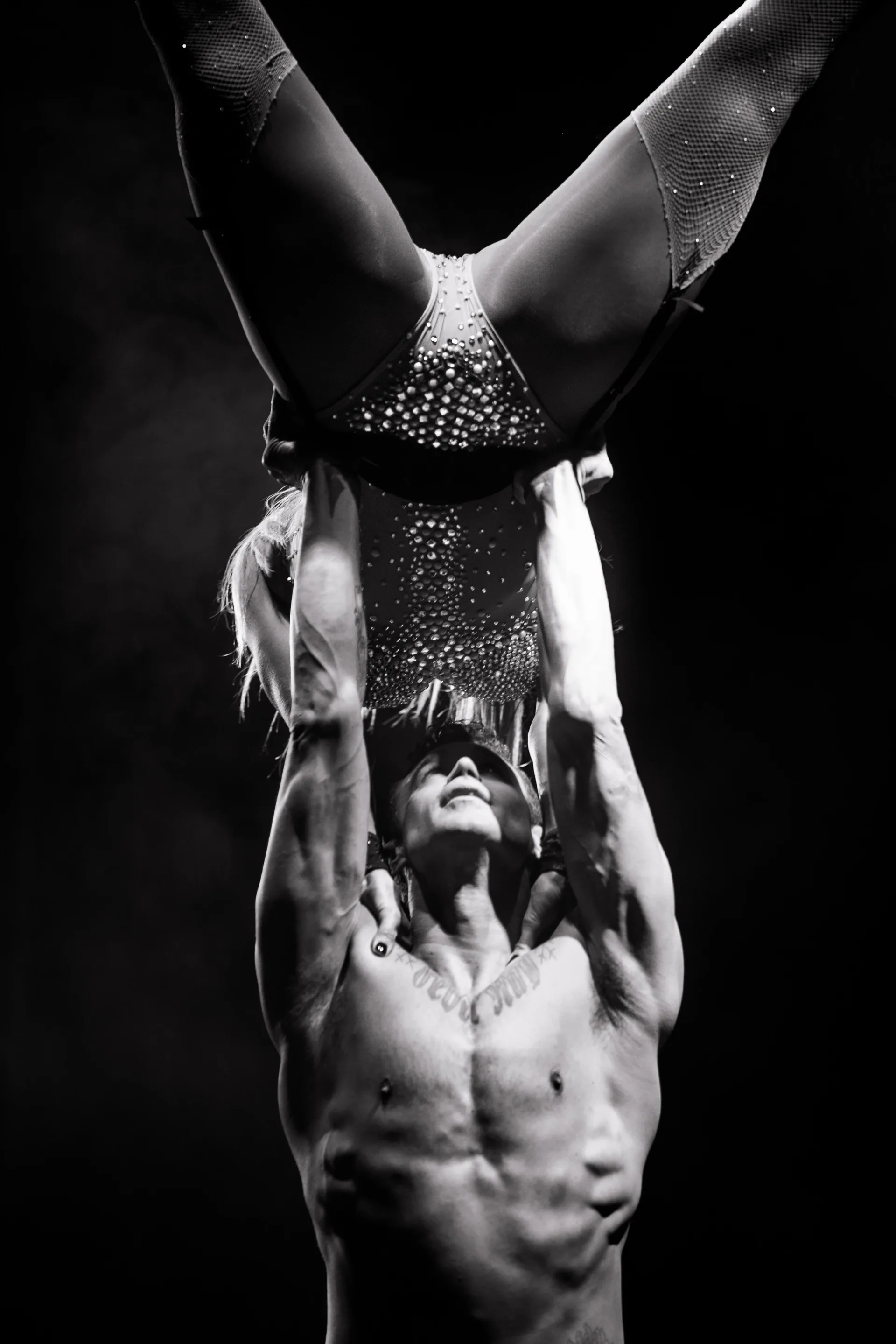 Two acrobats hold an inverted hand-to-hand balance beneath a spotlight.