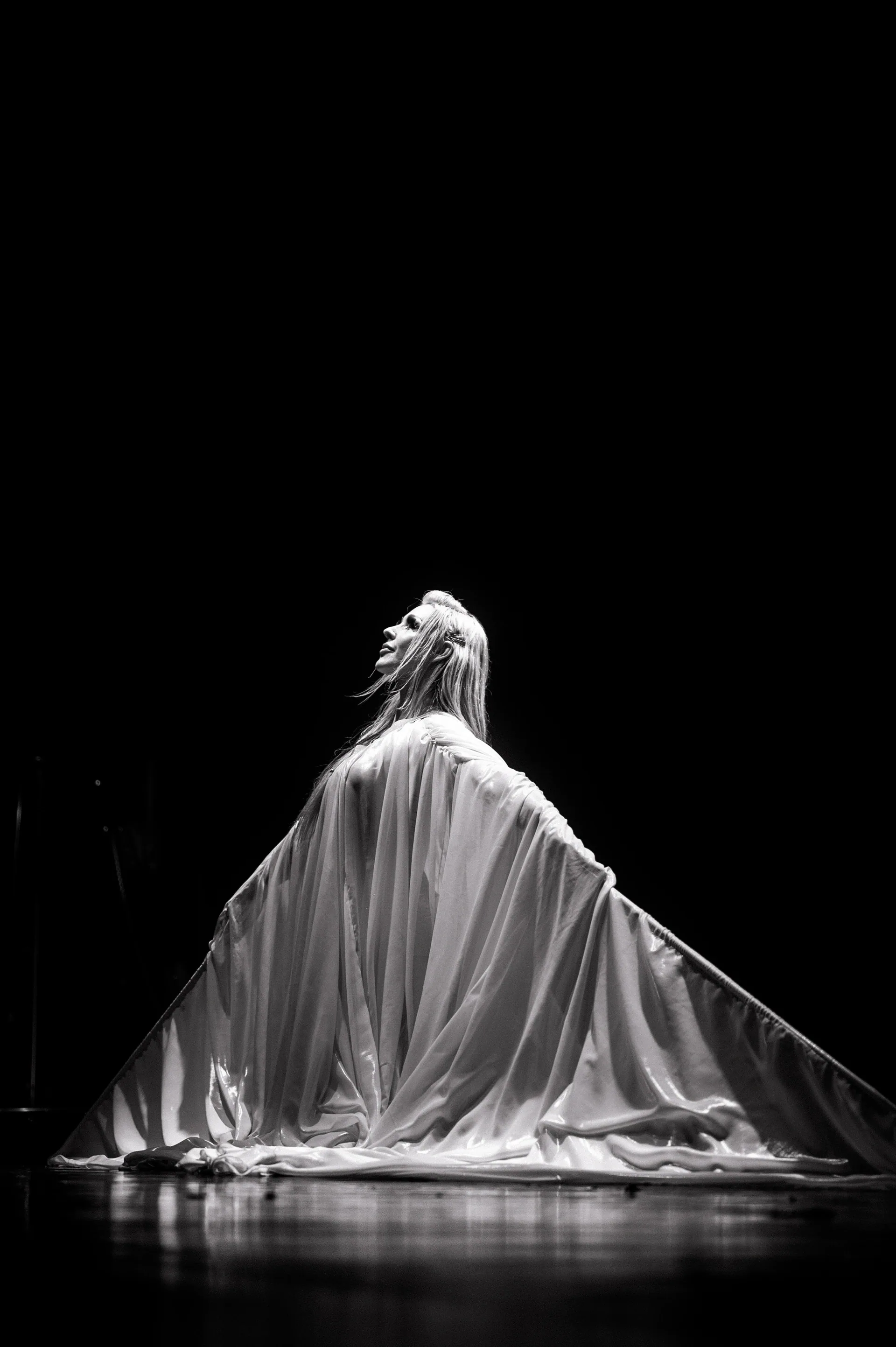 Performer sits beneath a broad sheet of fabric spread across the stage.