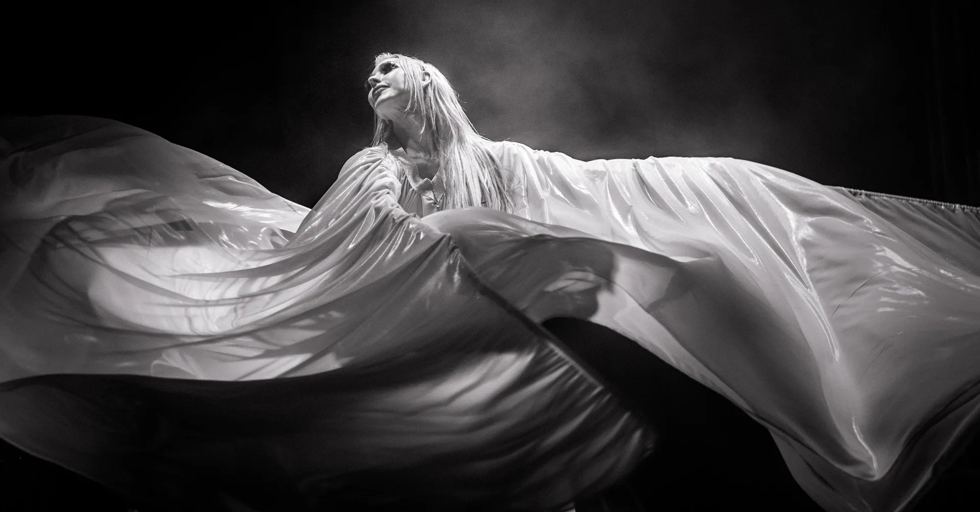 Performer extends both arms through a large expanse of flowing fabric.