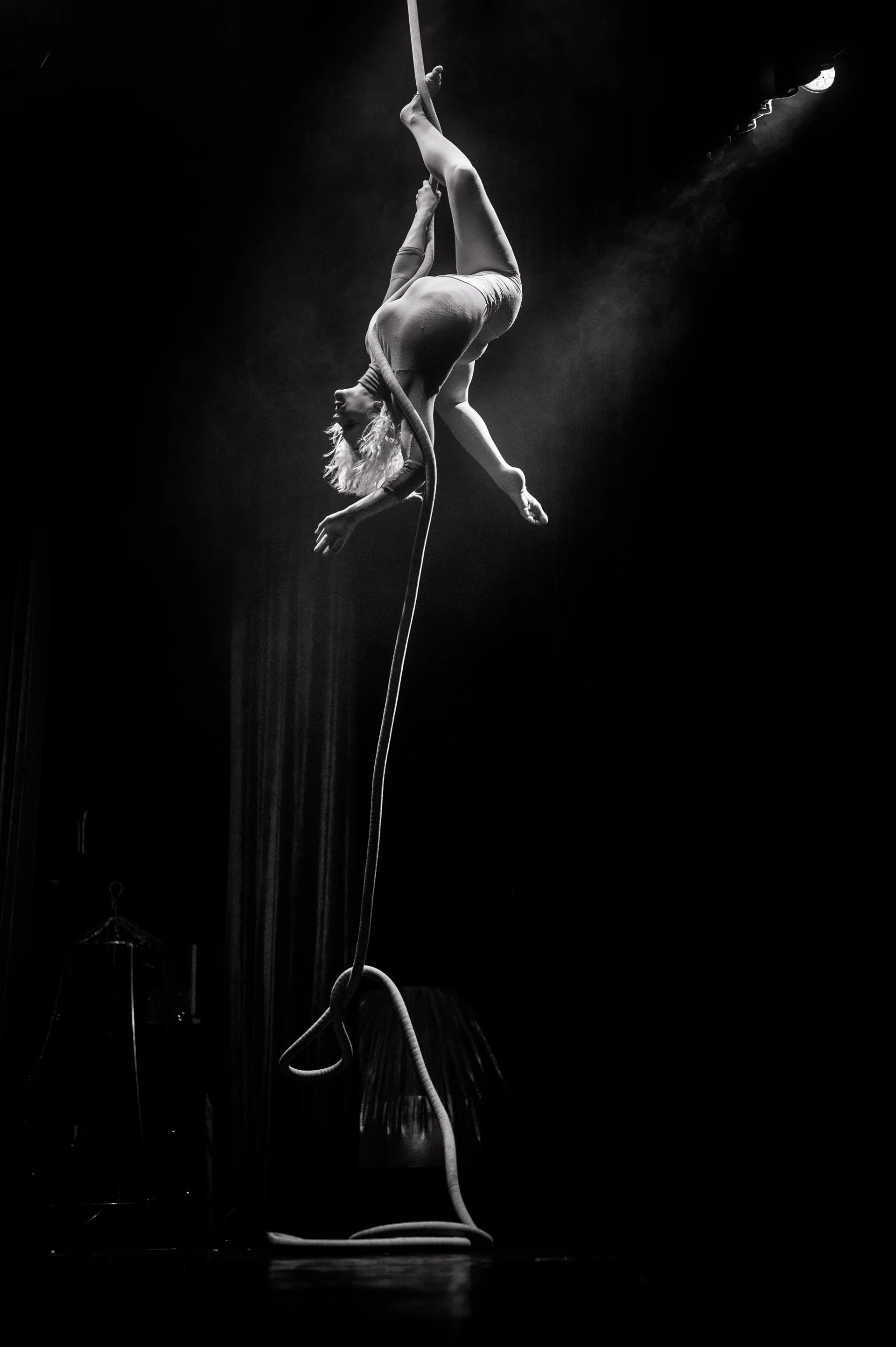 Aerial performer curls upside down around a vertical rope.