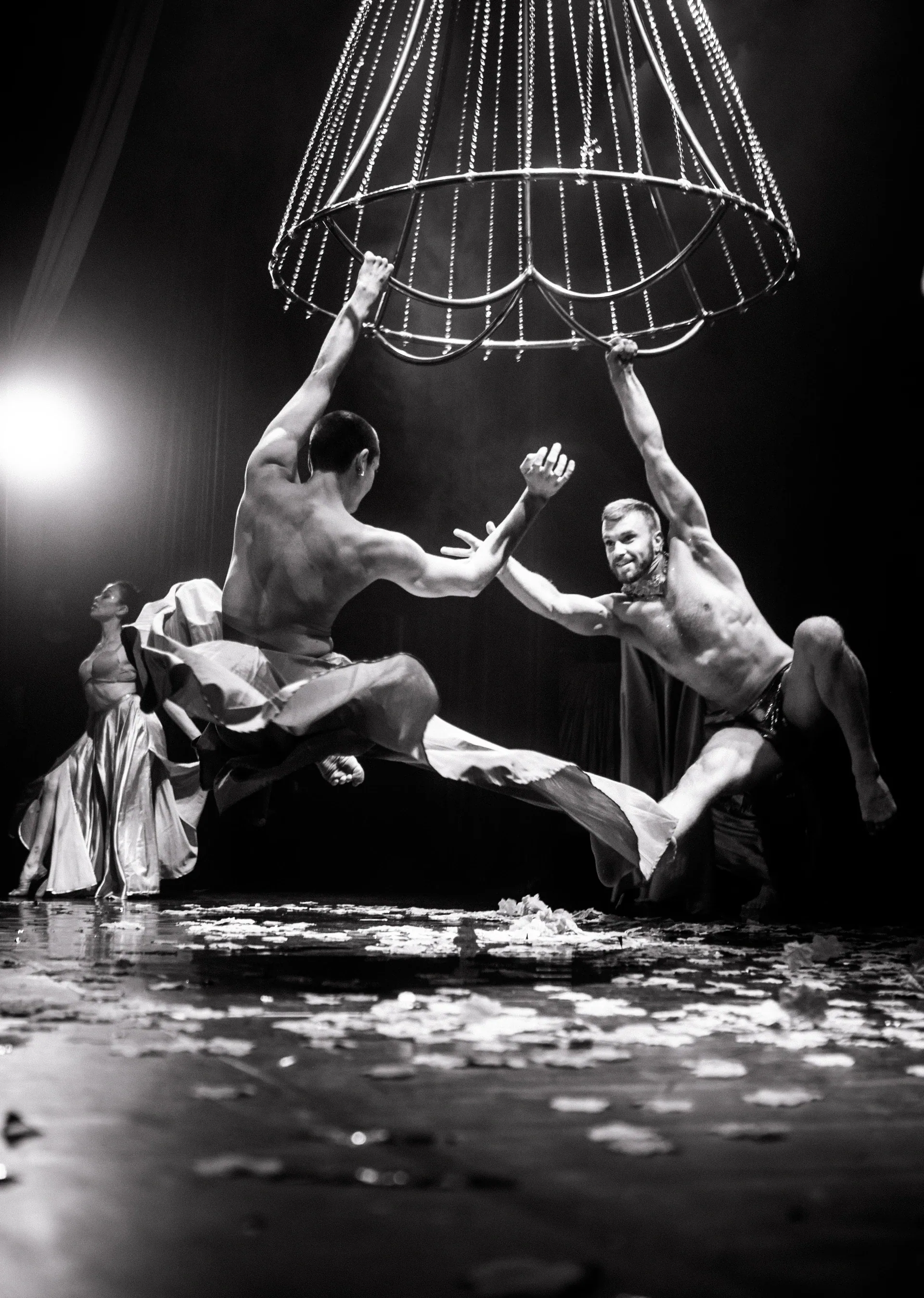 Group of performers lean and reach beneath a suspended cage-like frame.