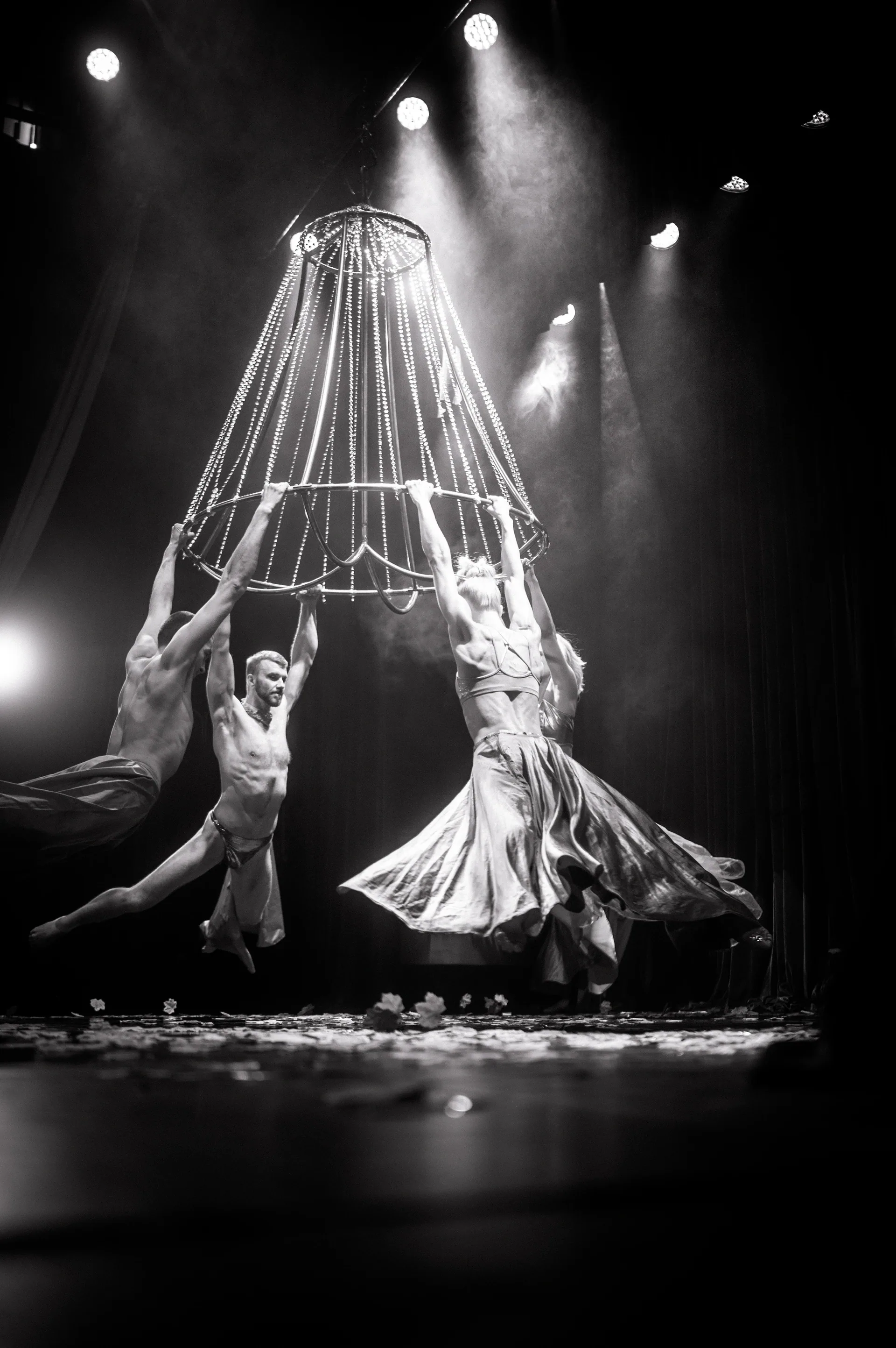 Two performers stand beside a suspended cage-like frame and trailing fabric.