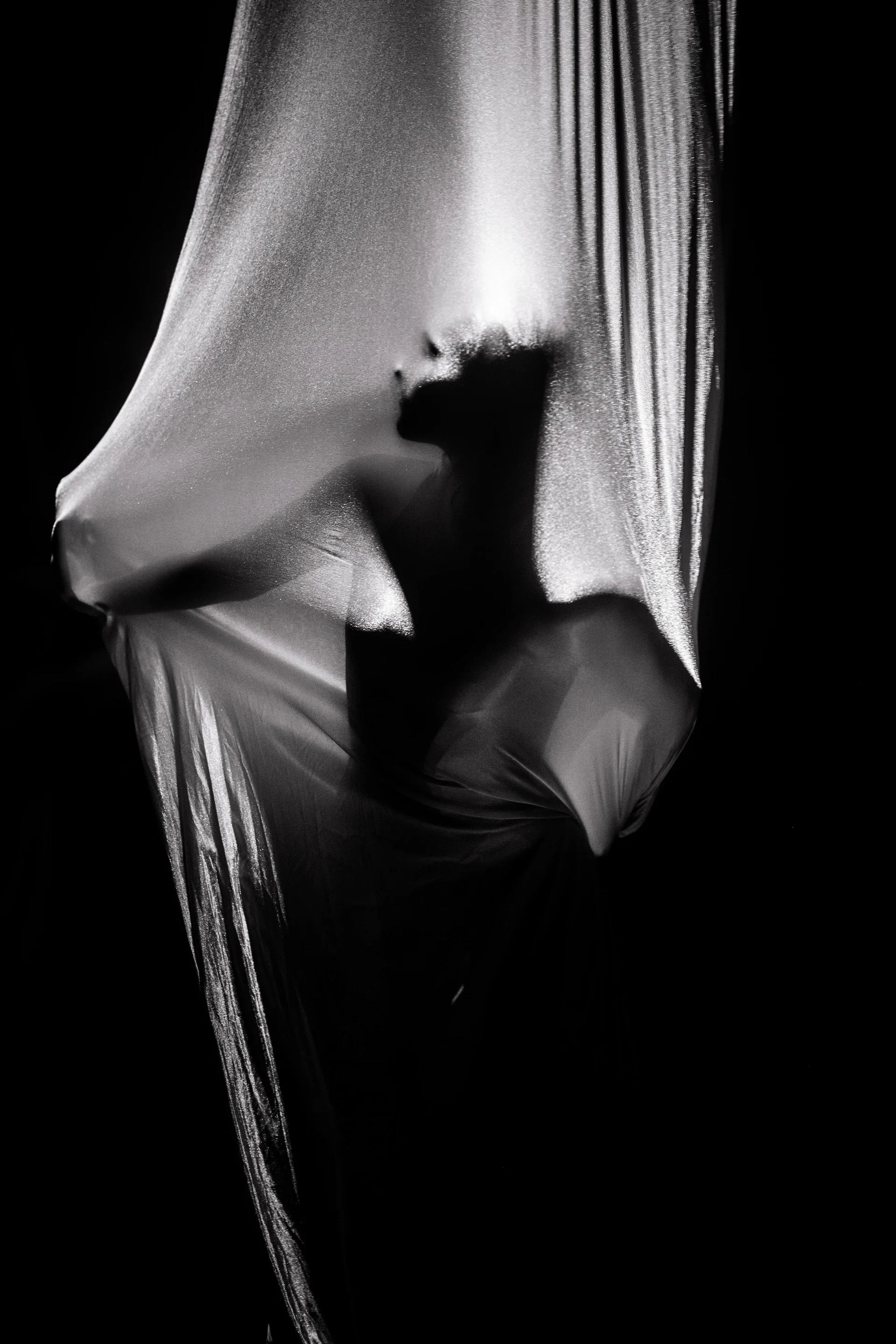Silhouette of a performer is visible inside pale aerial silk.