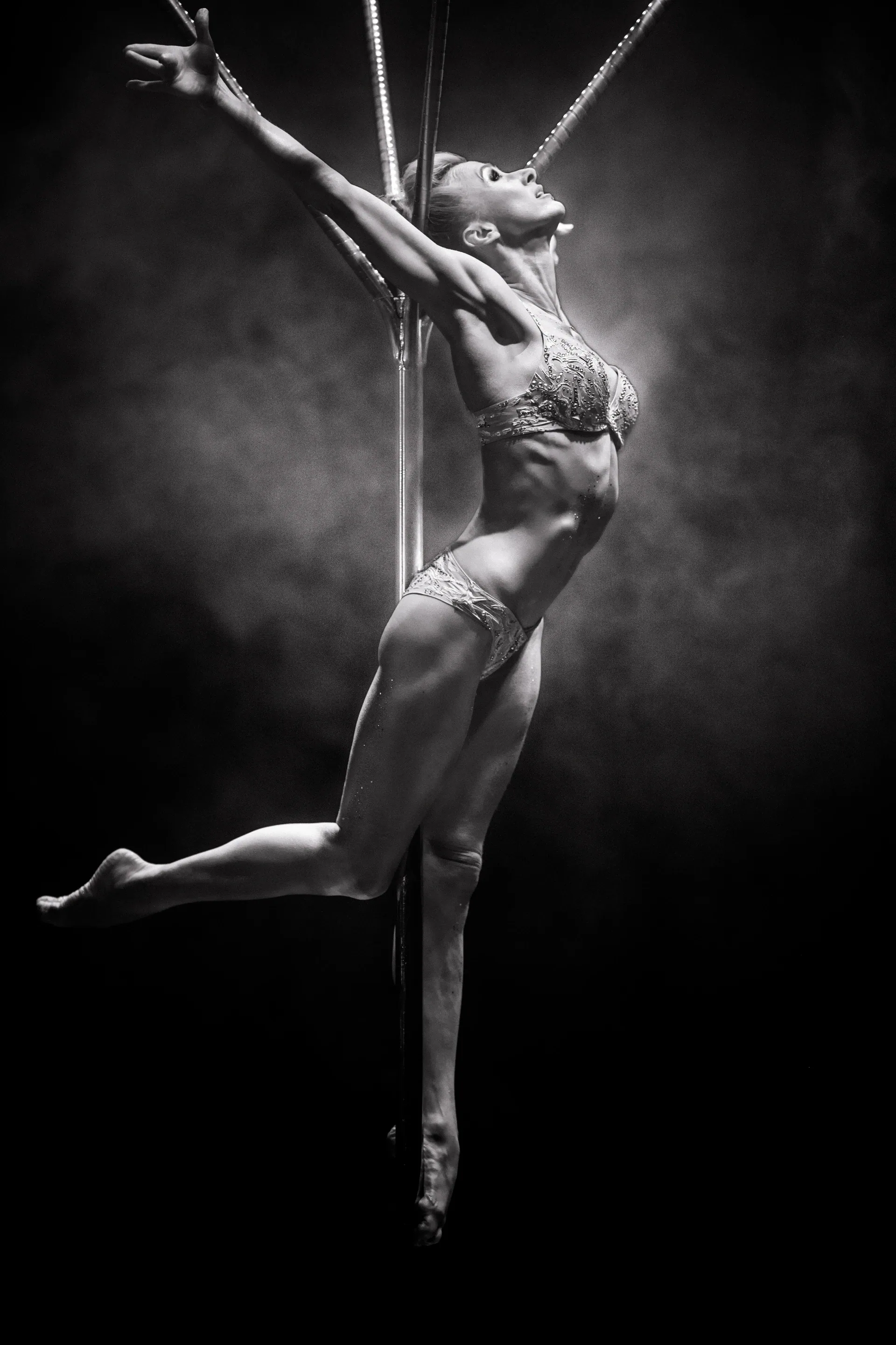 Aerial performer extends one leg while suspended from a vertical rope.