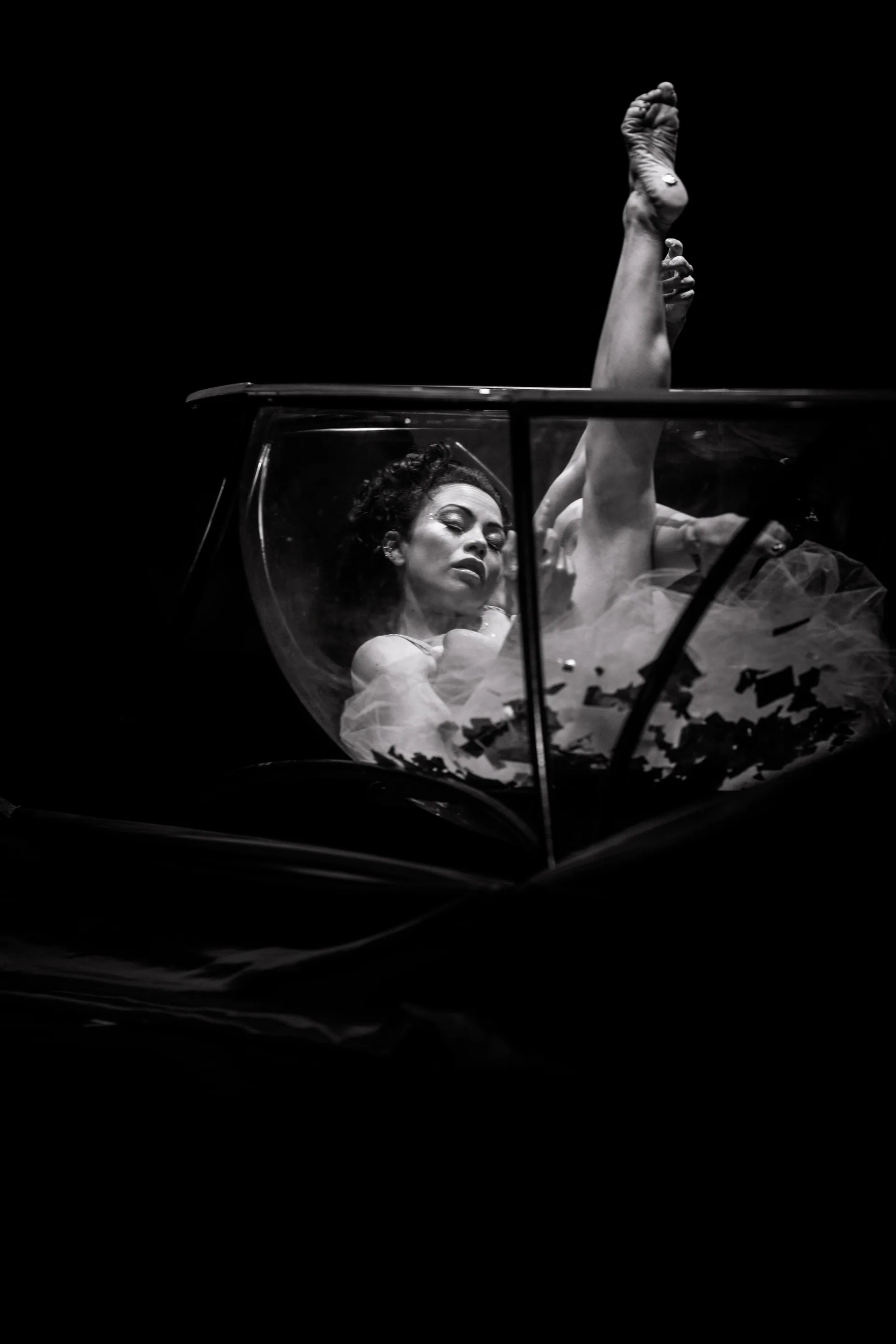 Performer emerges from a transparent tank with one leg raised vertically.