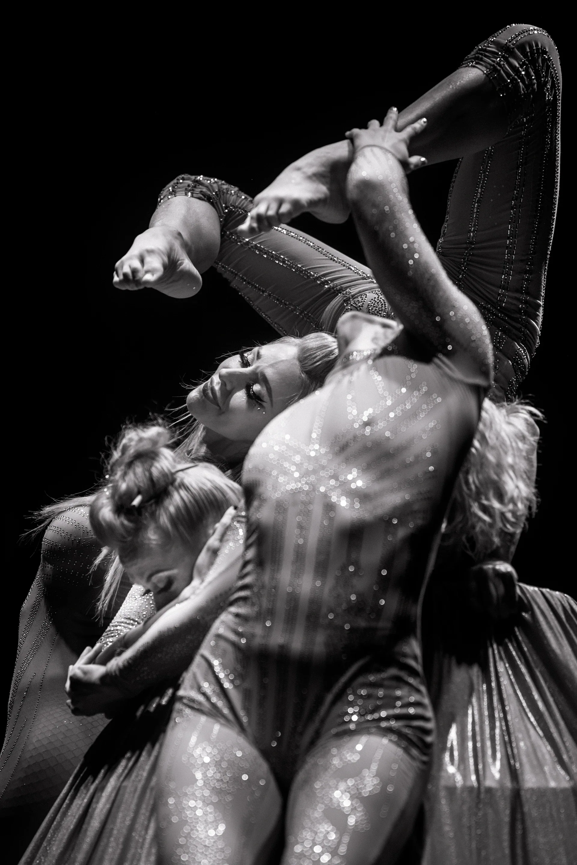 Two performers in reflective costumes hold a close intertwined contortion pose.