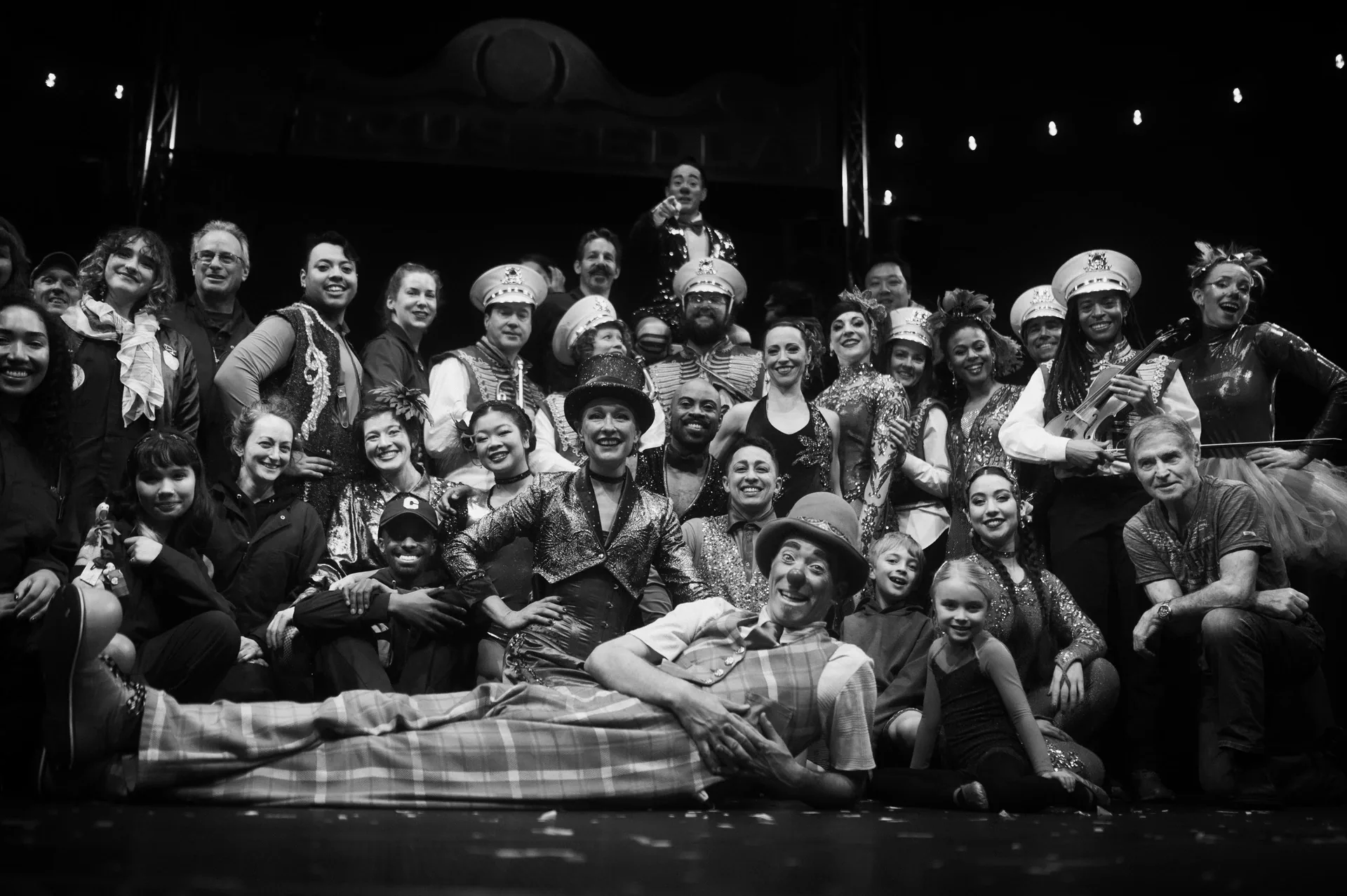 Large ensemble of circus performers poses together across the stage.