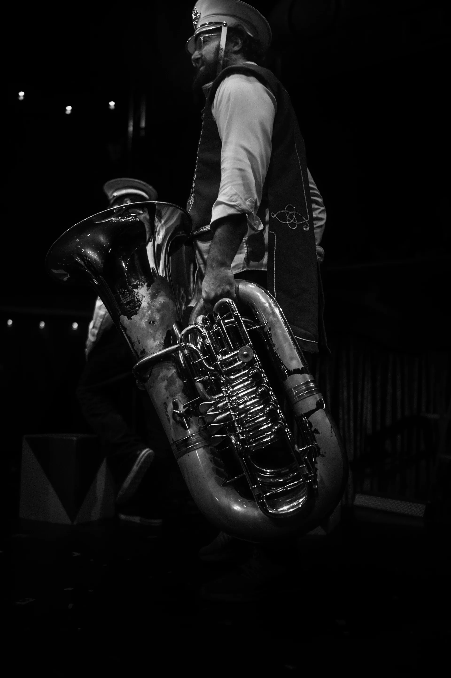 Musician stands holding a large tuba at the side of the stage.