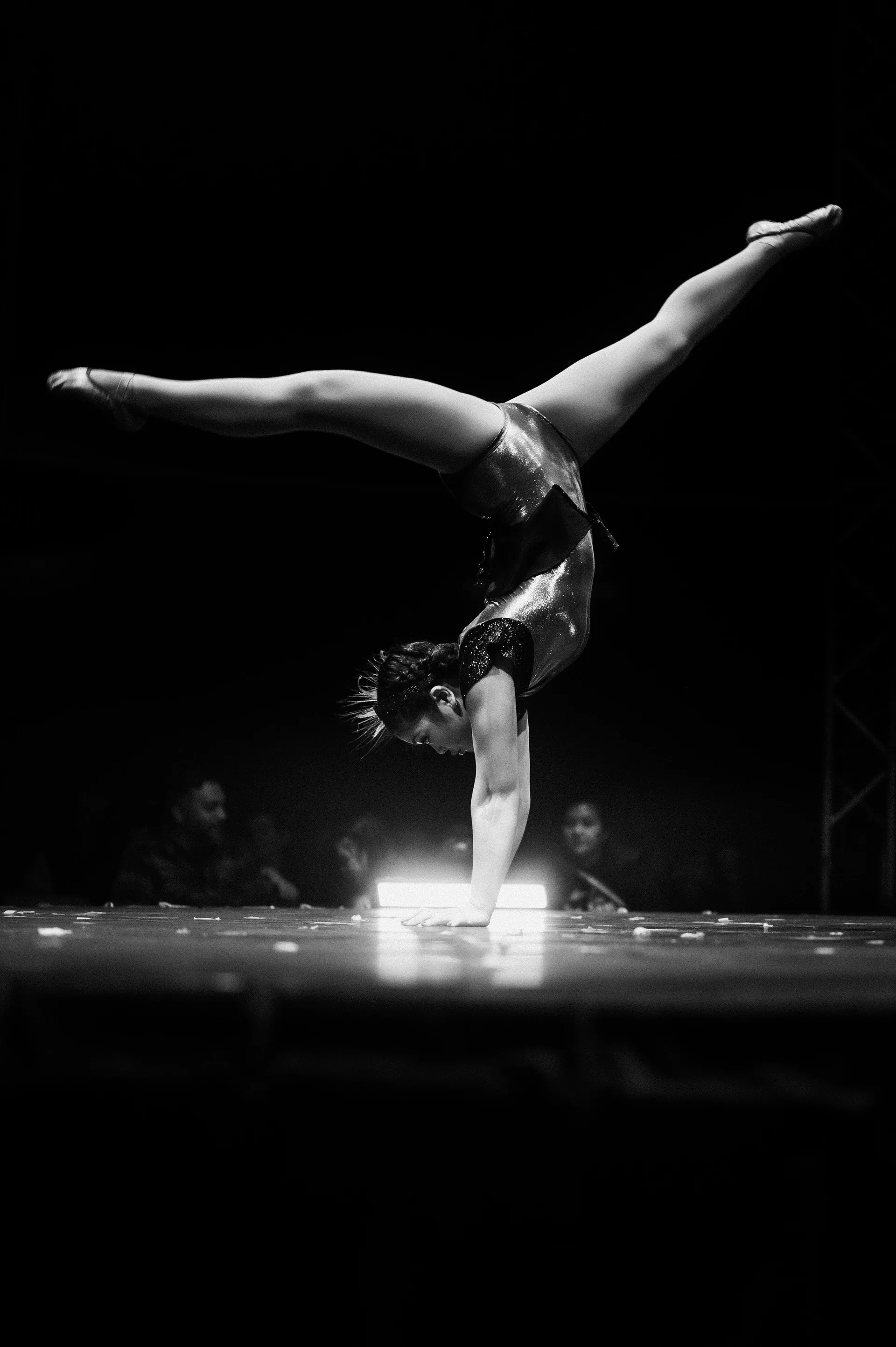 Acrobat balances in a one-handed handstand on the stage.