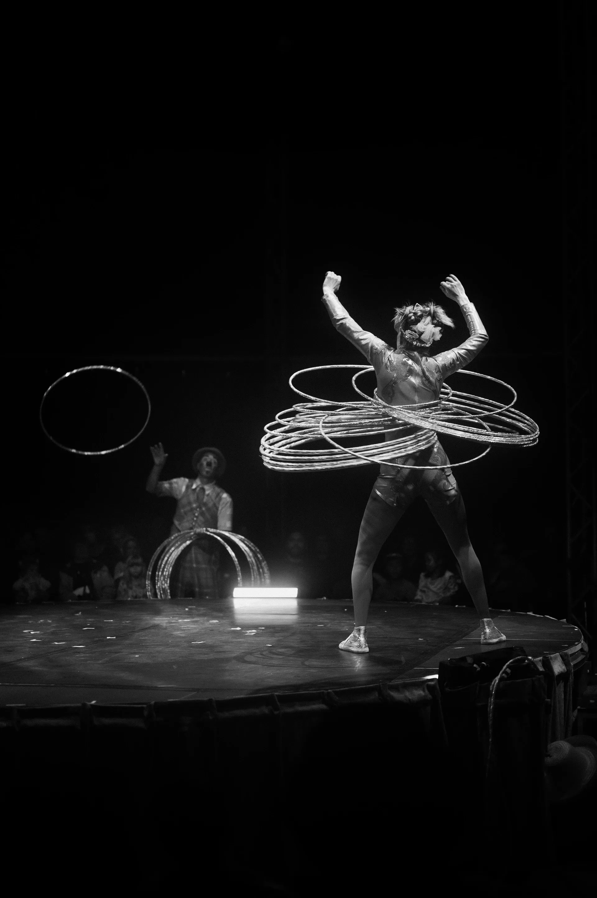 Performer spins several hoops around the body on a circular stage.