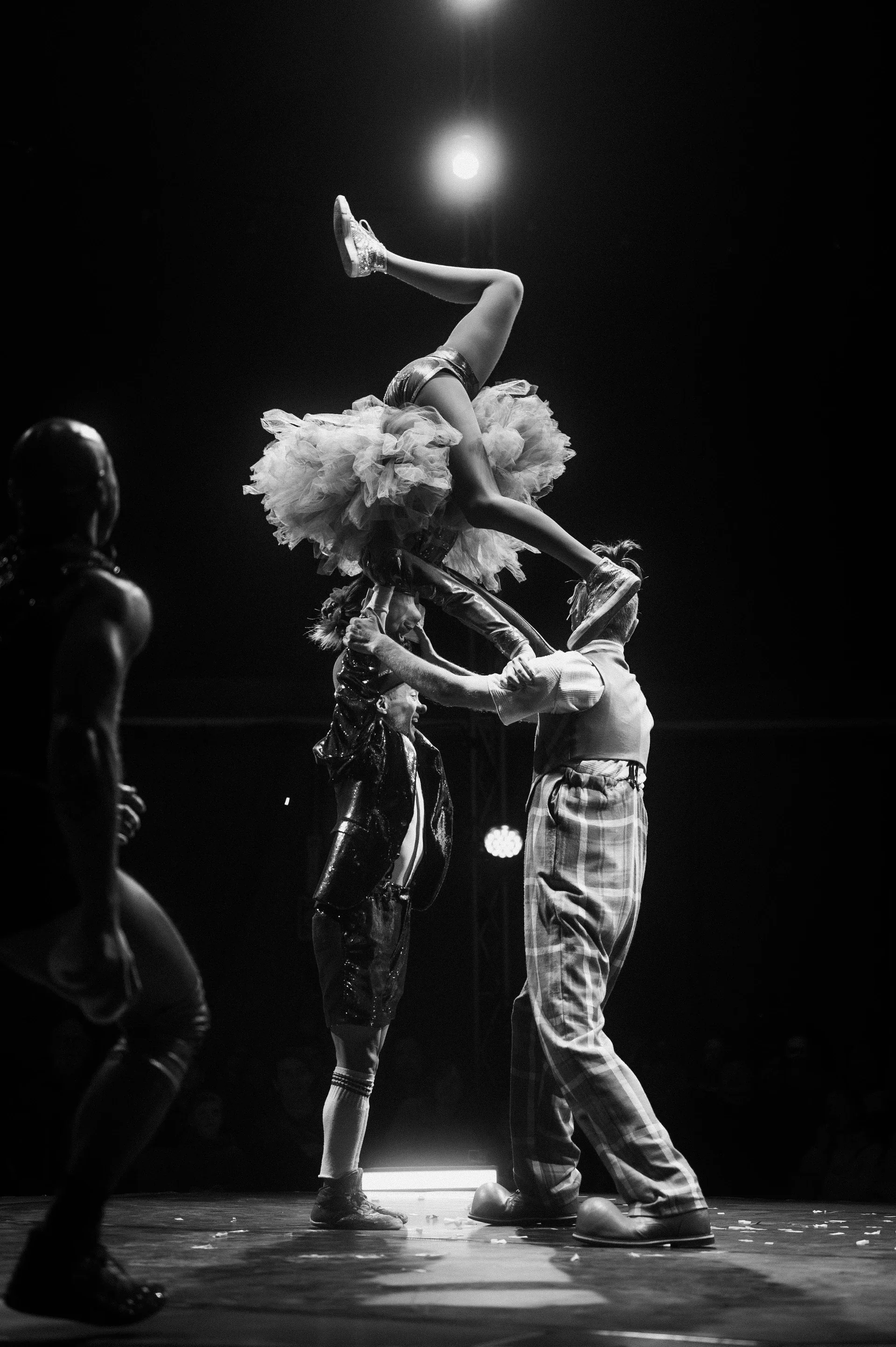Two performers execute an acrobatic lift beneath a spotlight.