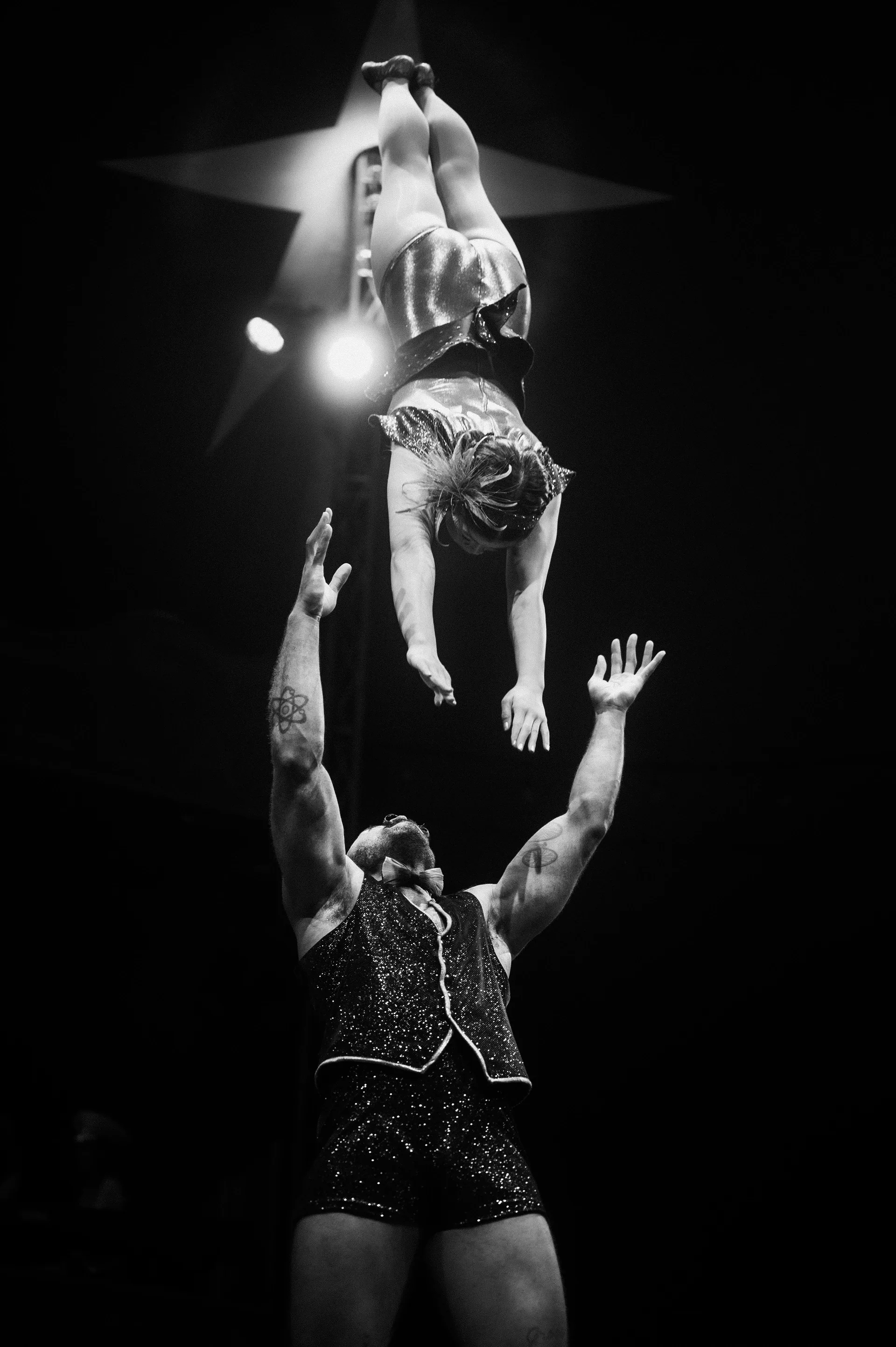 One acrobat holds another upside down above outstretched hands.