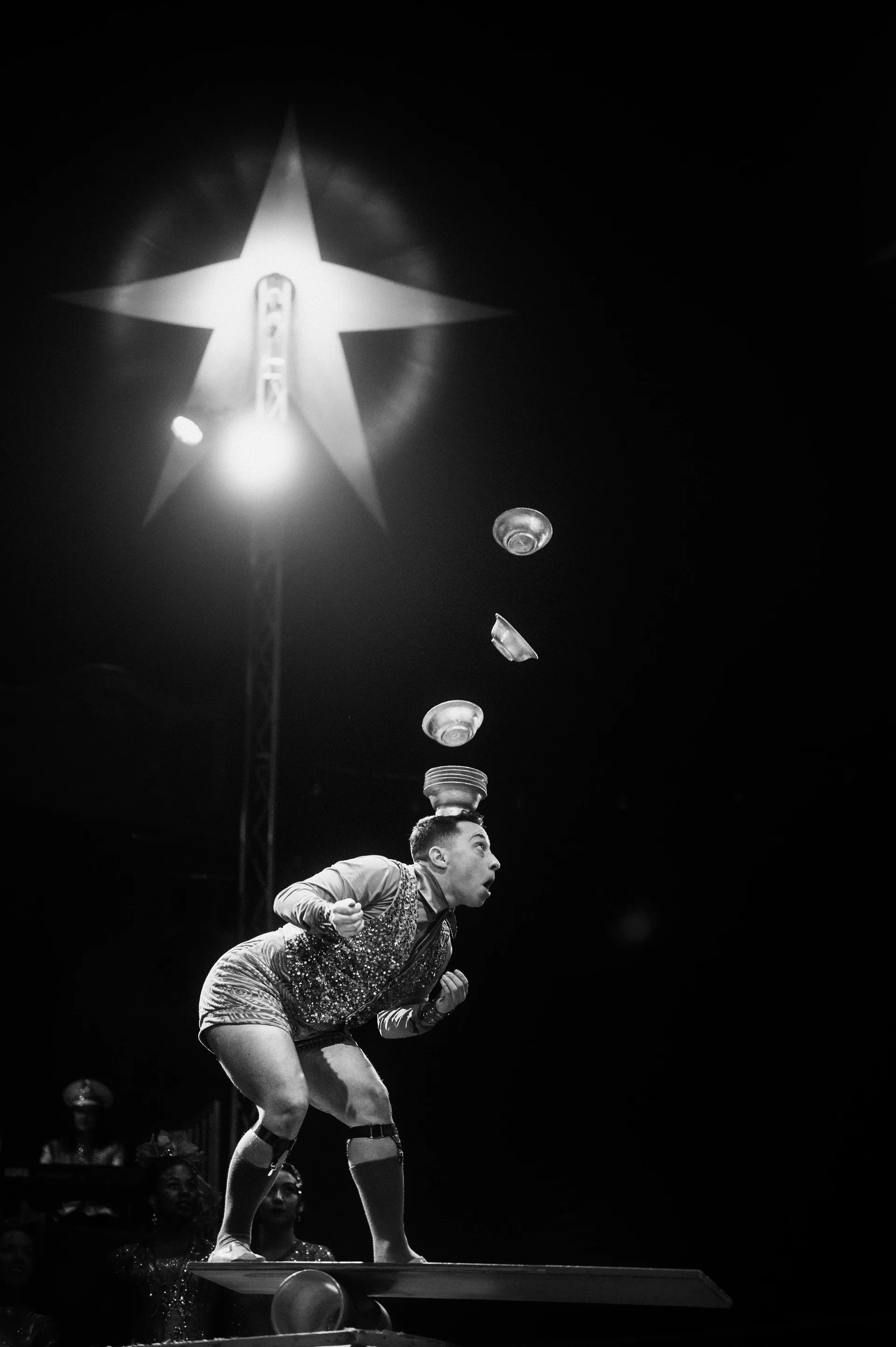 Juggler bends forward while several balls arc overhead.
