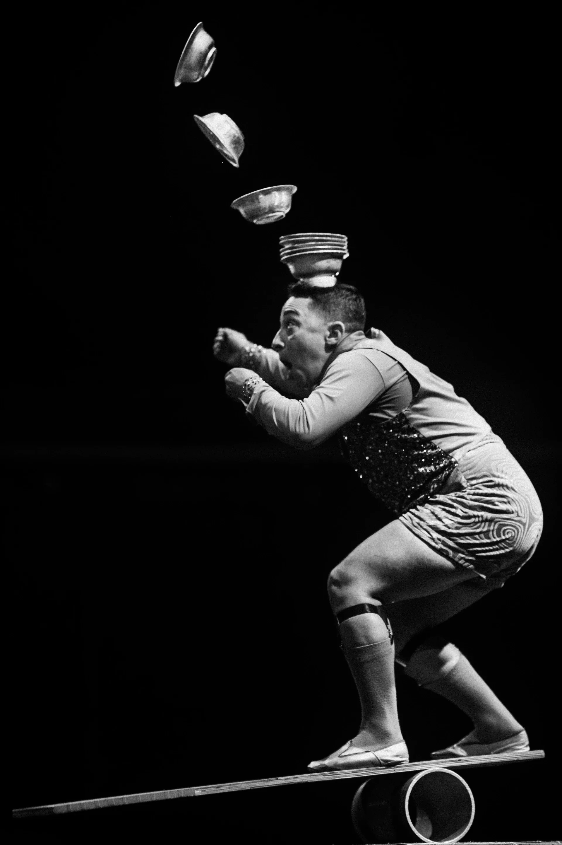 Performer balances on a board over a cylinder while juggling.