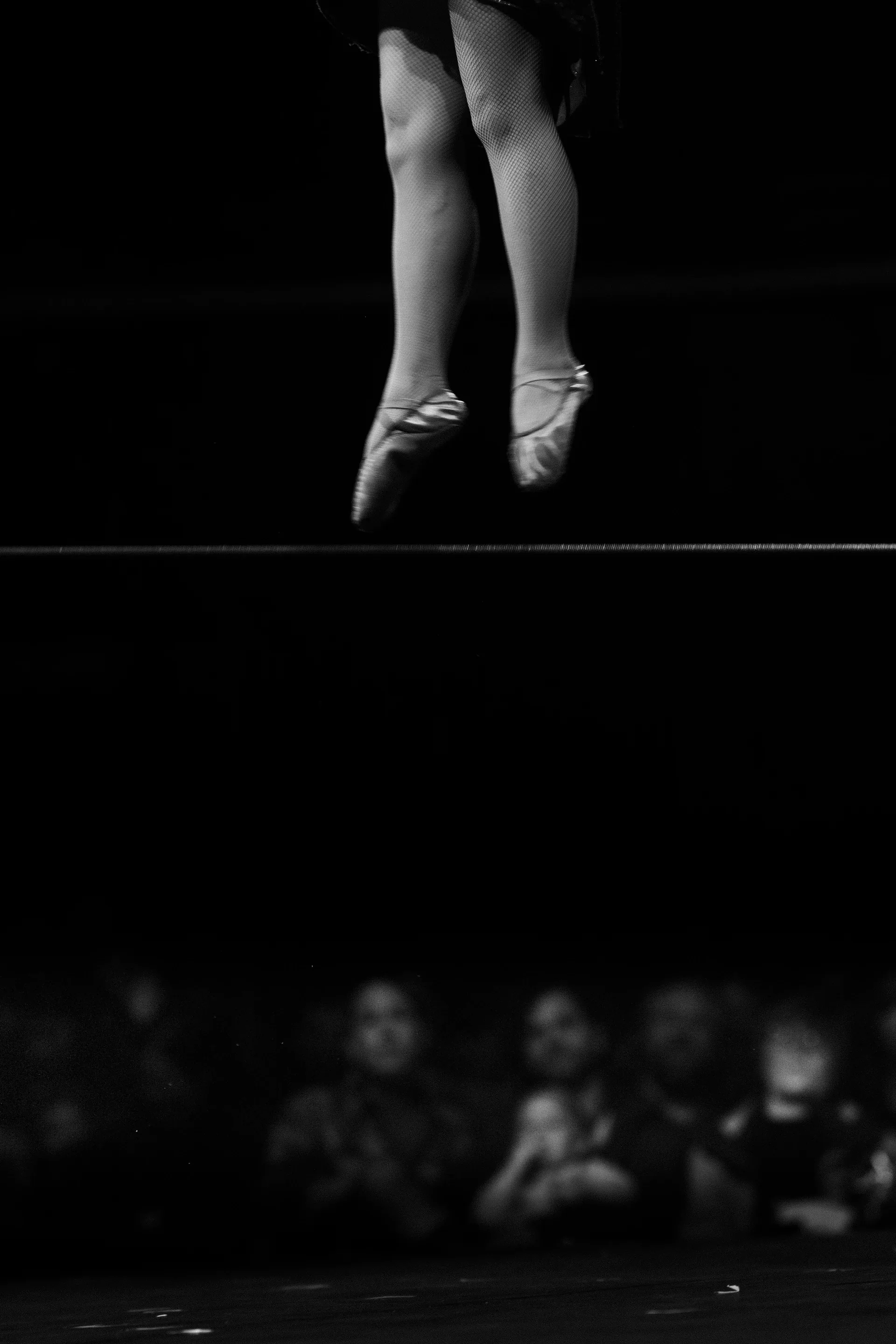 Bare feet hover above the stage with the audience blurred behind.