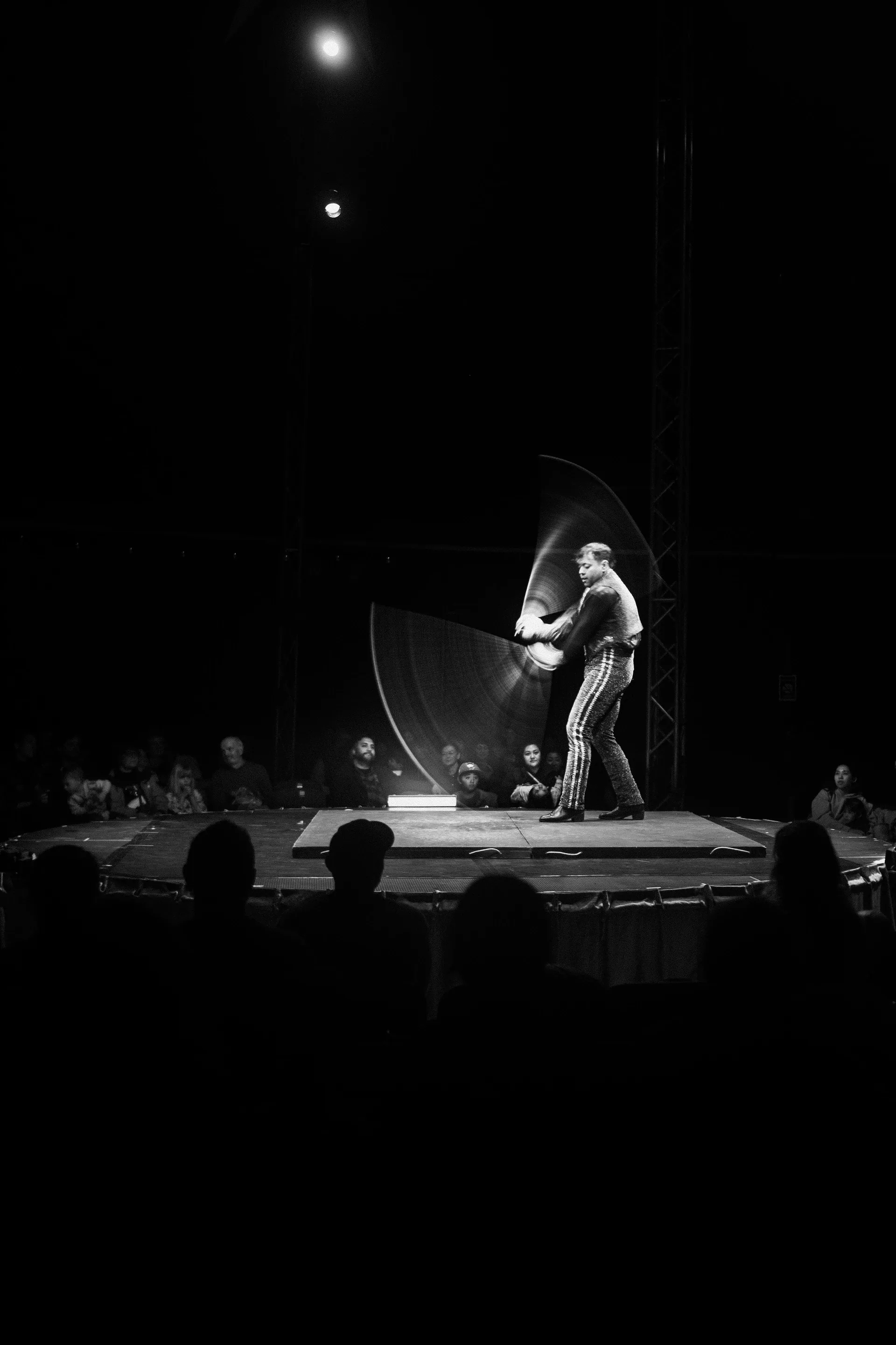 Performer spins two large fan-like props while standing on a raised stage.