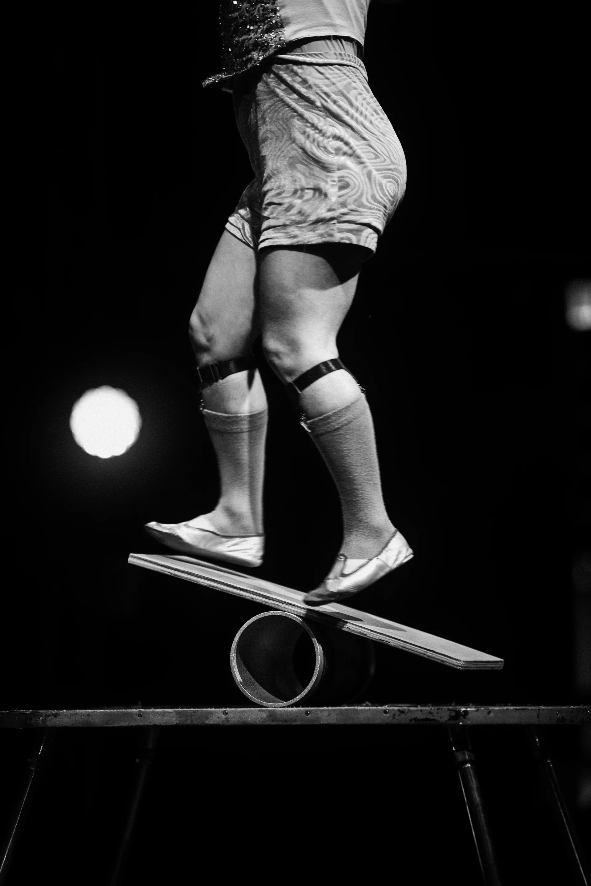 Close view of a performer's feet balancing on a board over a cylinder.