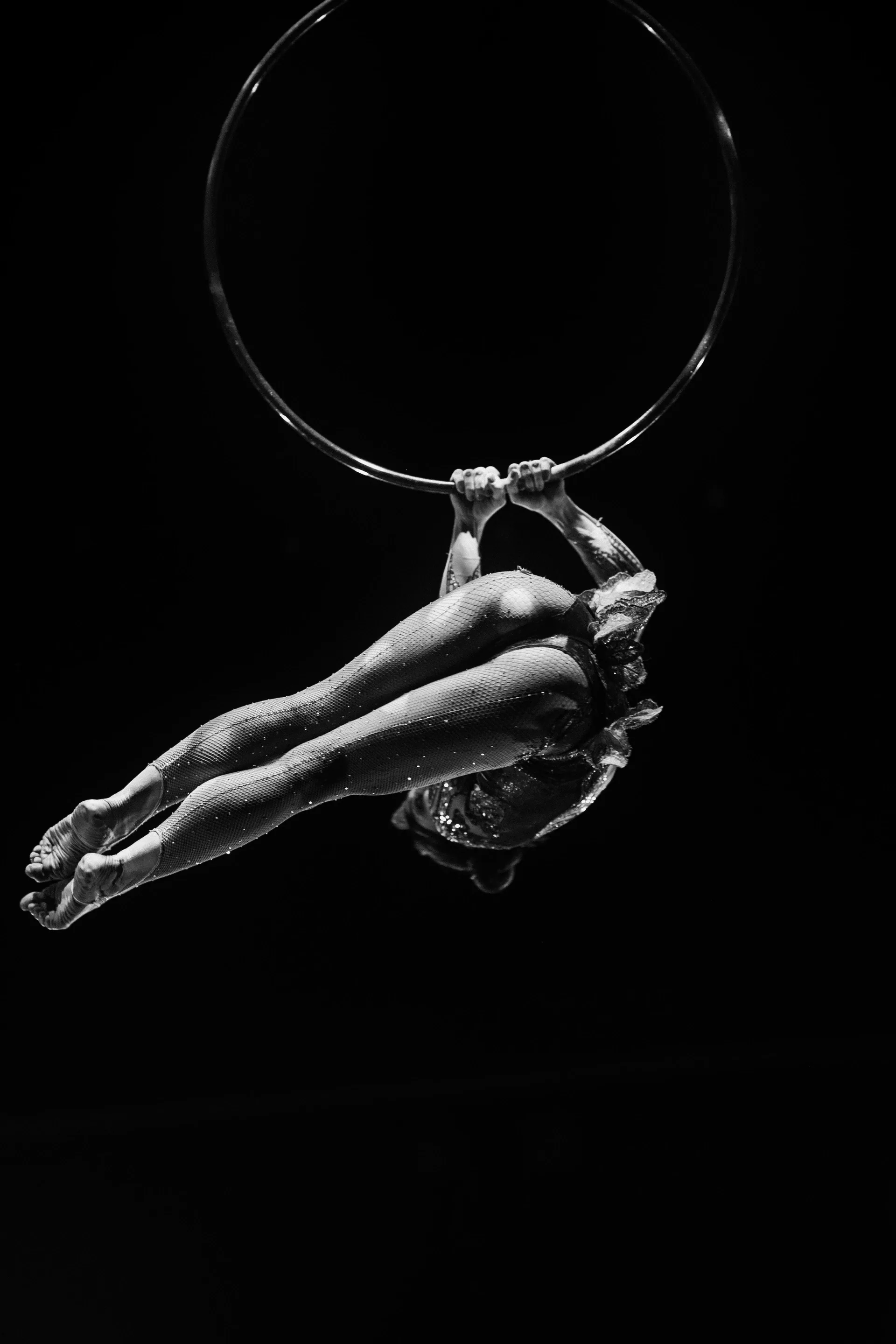 Two aerialists recline together inside a large suspended hoop.