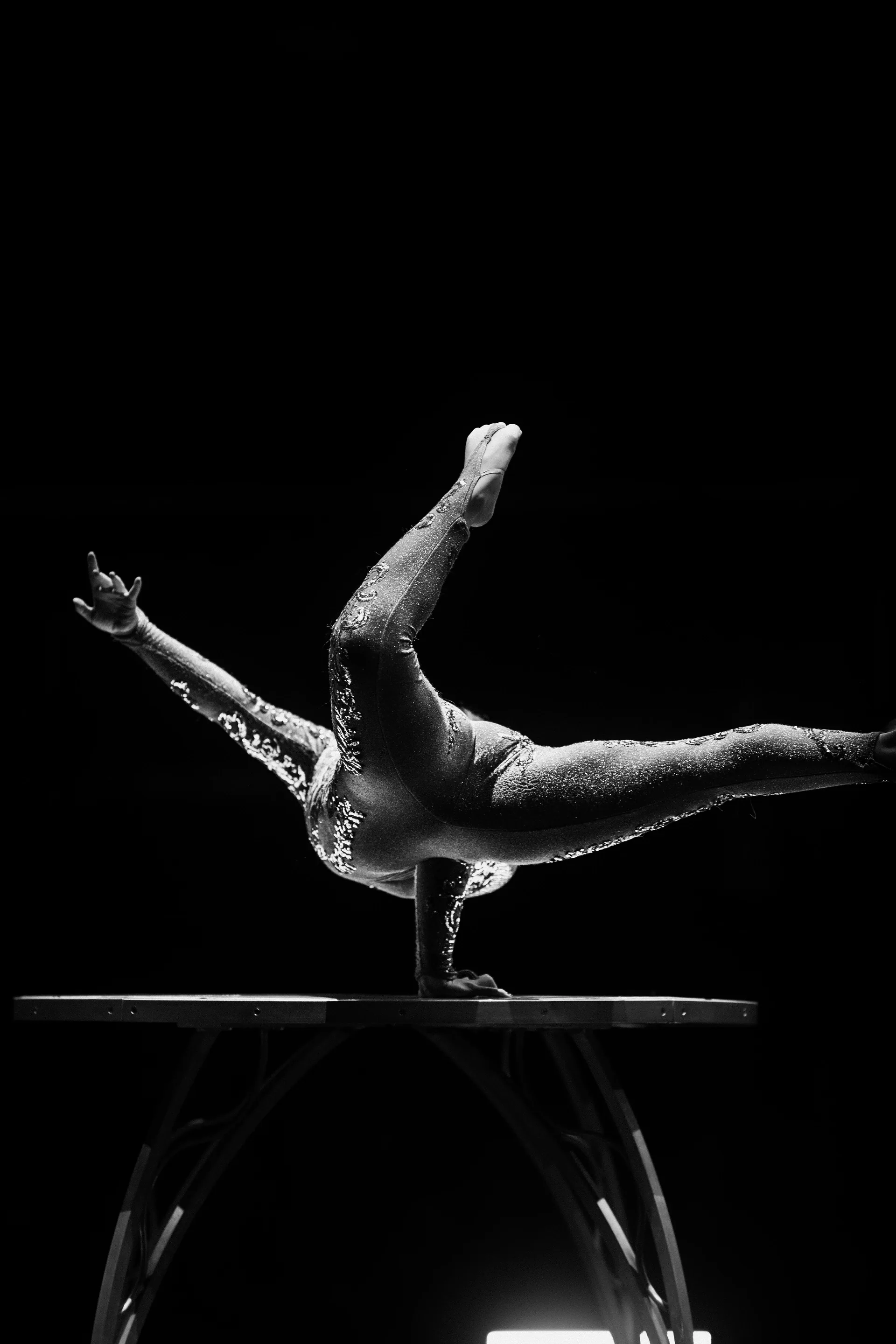 Acrobat holds a horizontal balance on the hands atop a low platform.