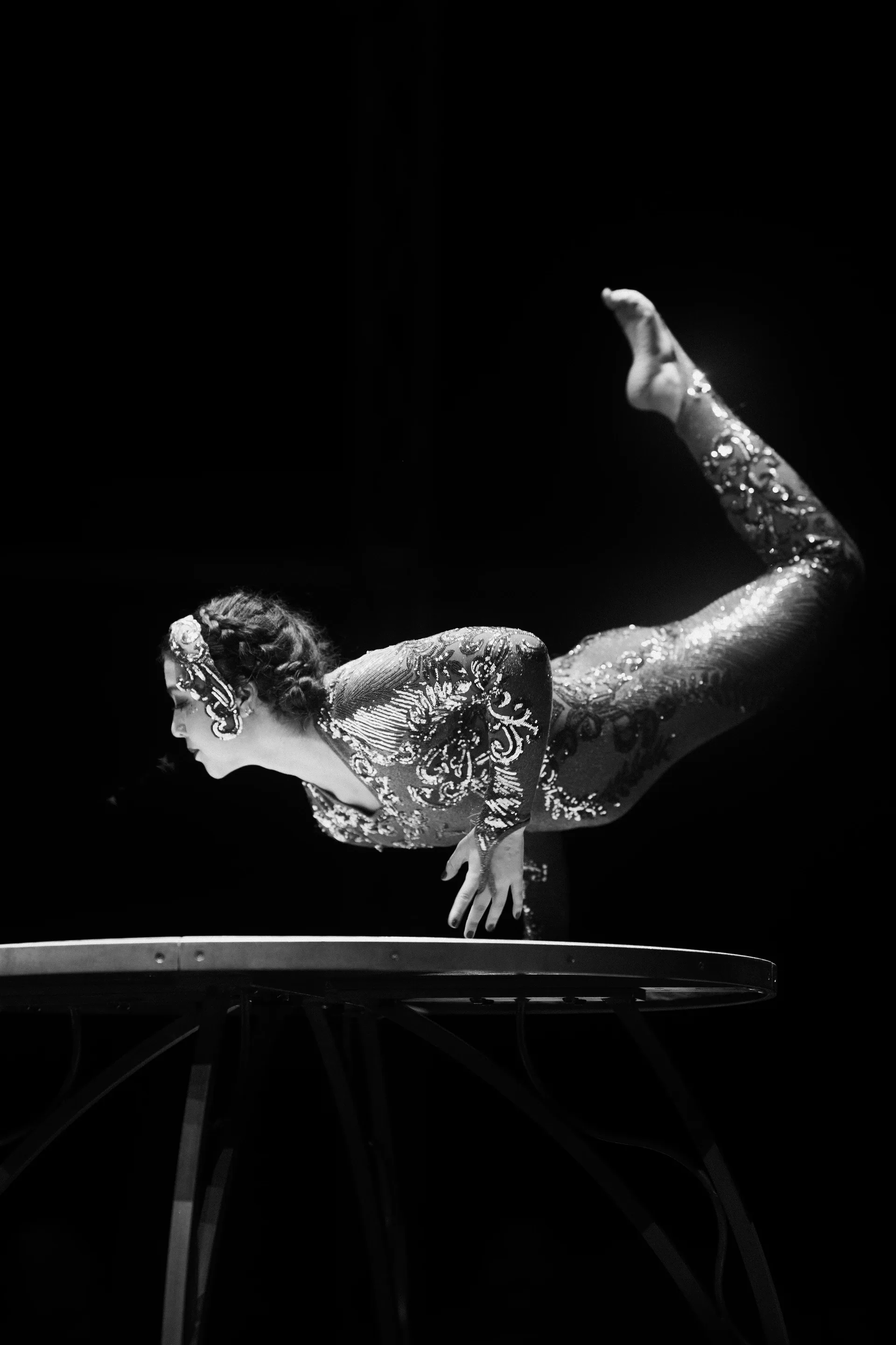 Contortionist balances on both hands with legs bent overhead.