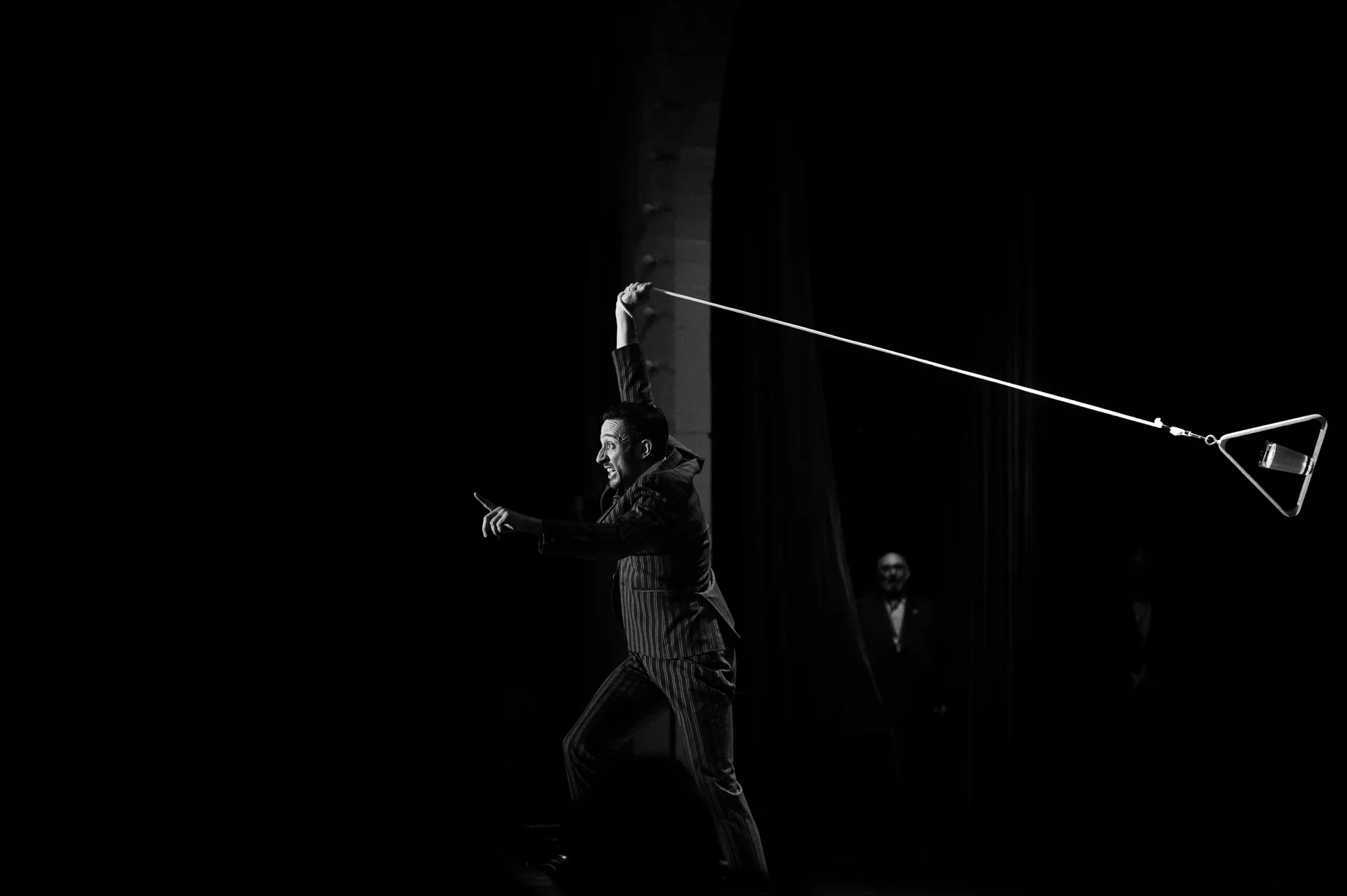 Performer stretches a long whip across the dark stage.