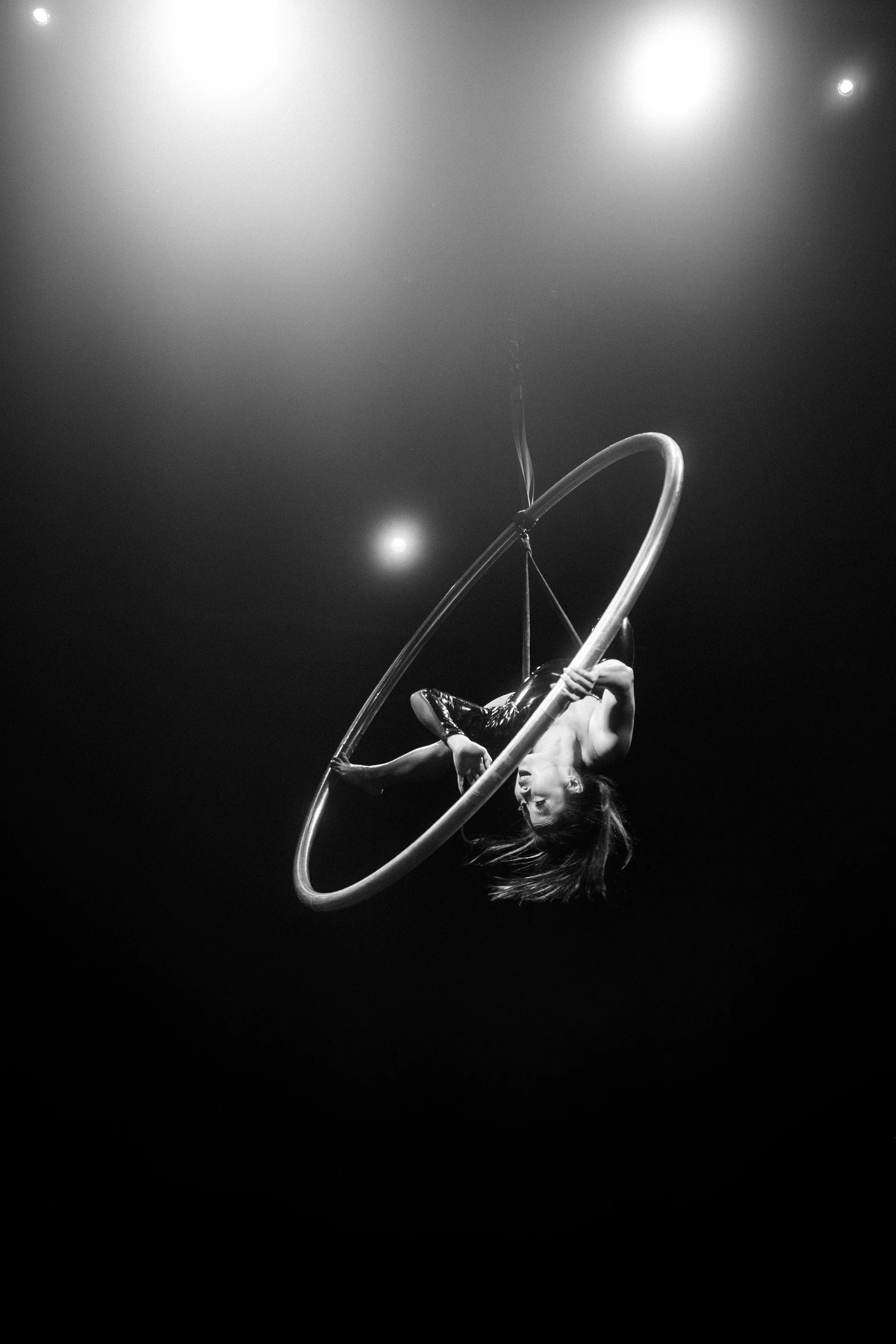 Aerialist curls inside a hoop beneath stage lights.