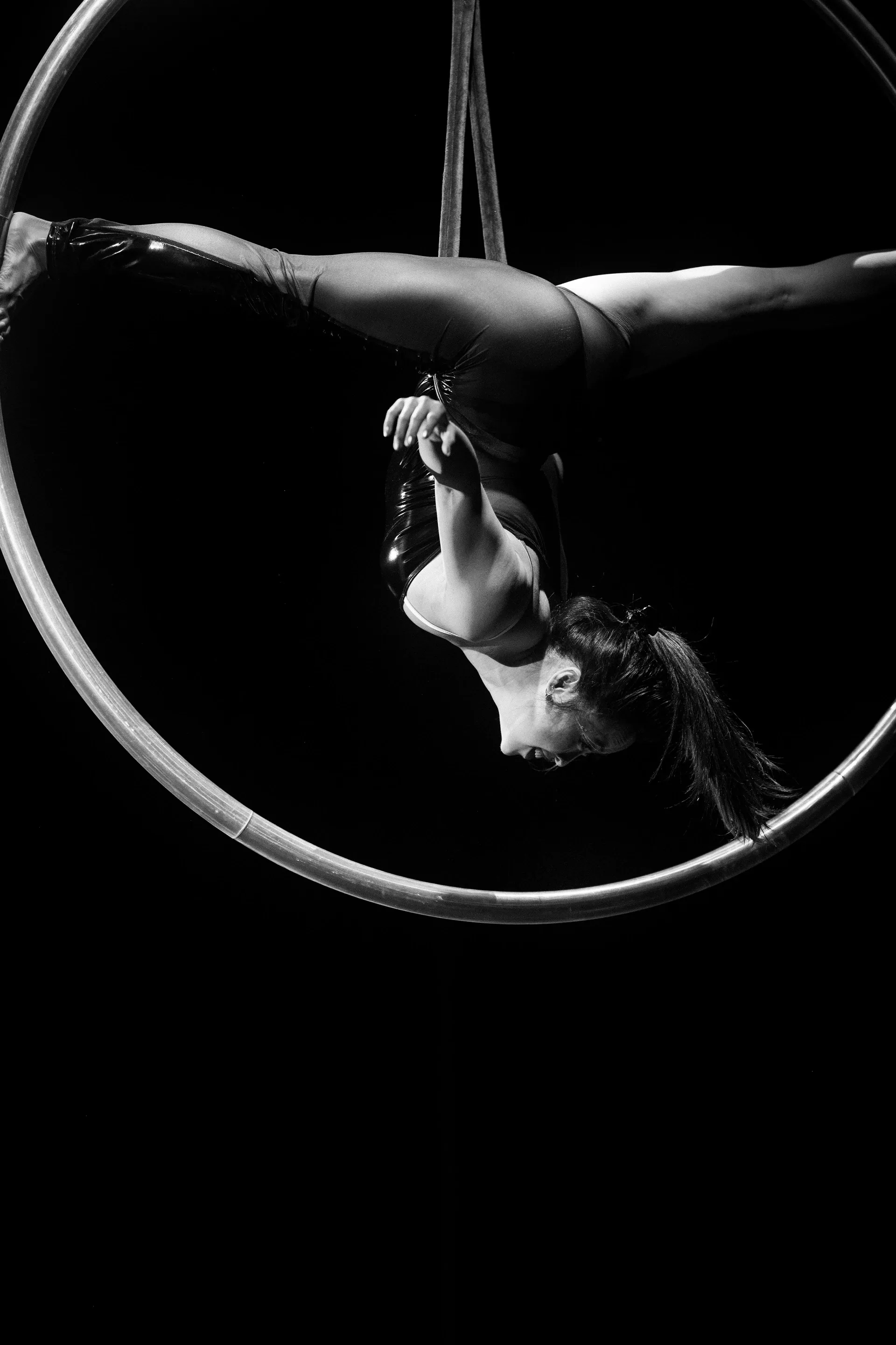 Close view of an aerialist draped over a hoop with arms hanging downward.