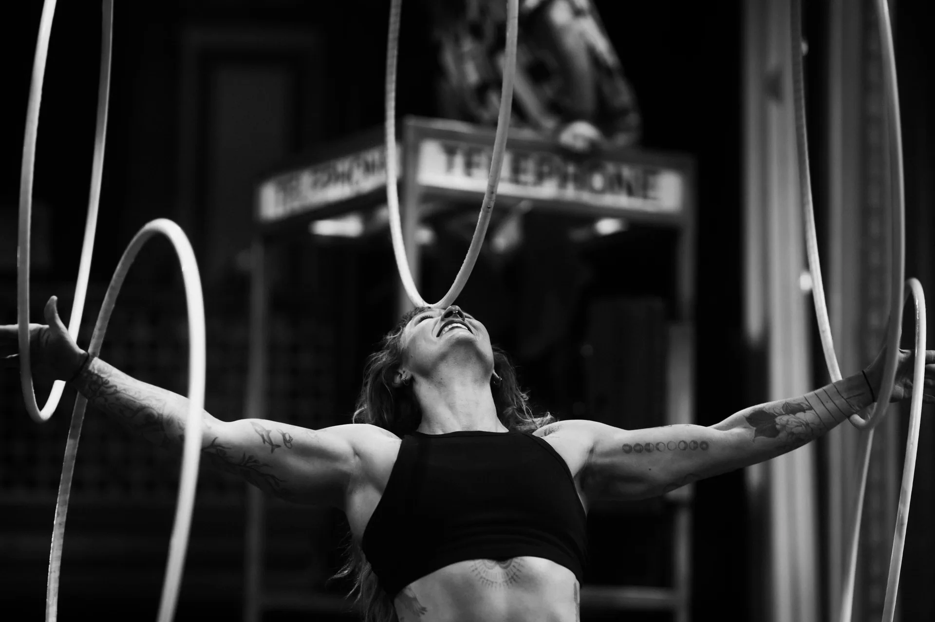 Performer stands with arms extended while holding several hoops.
