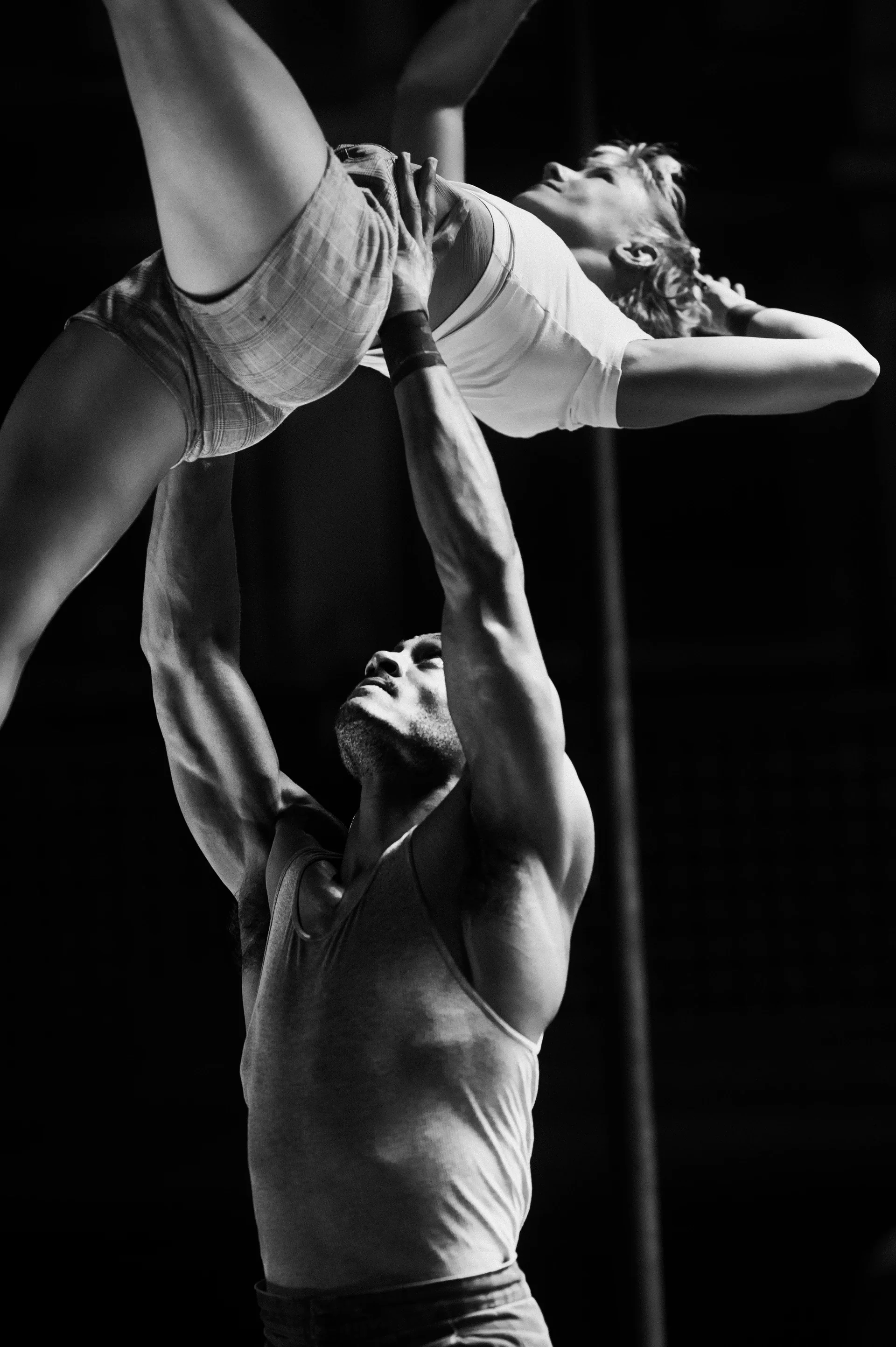 Acrobatic pair holds an overhead balance with one performer supported at the hips.