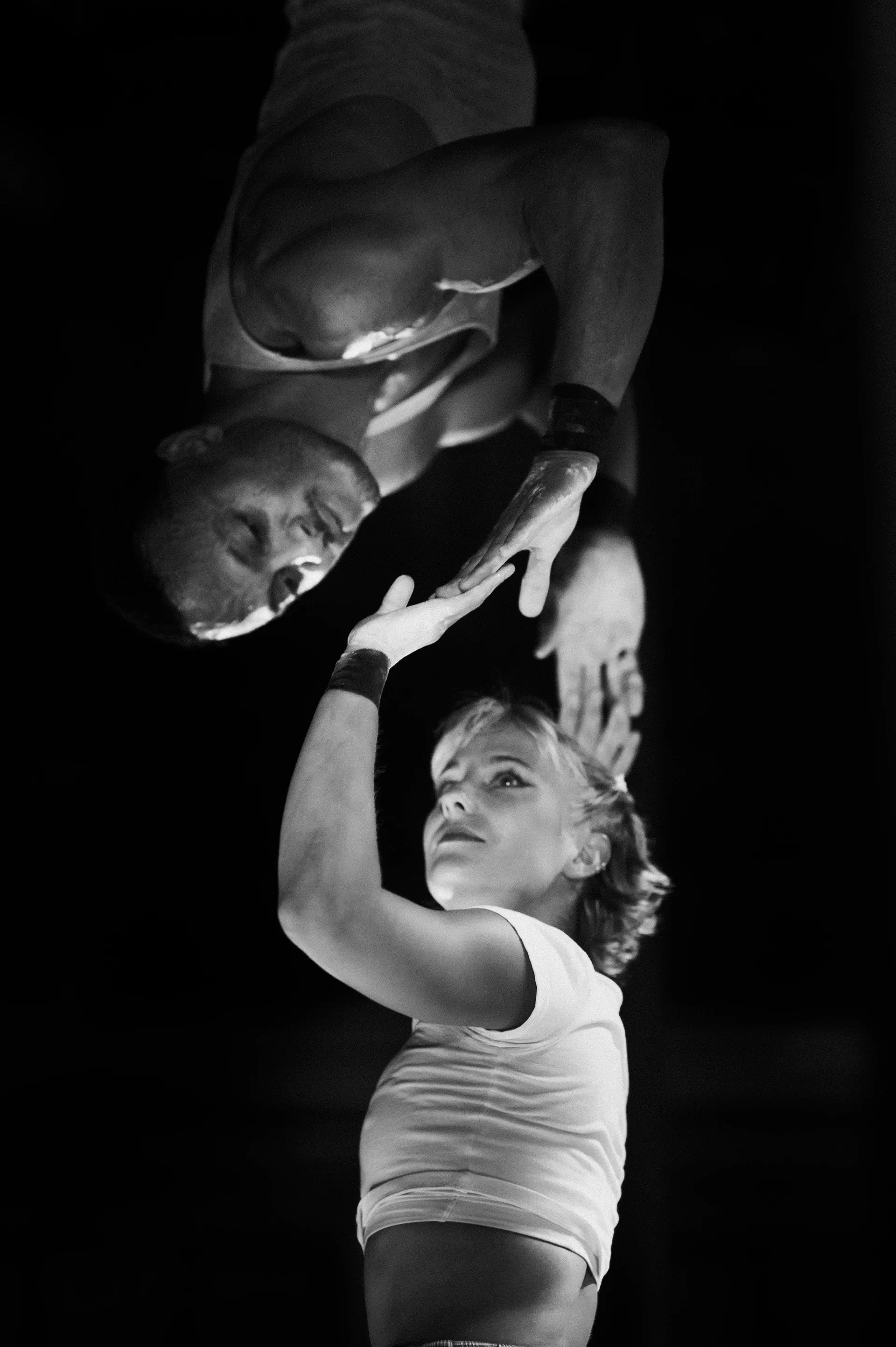 Inverted performer reaches toward a standing partner below.
