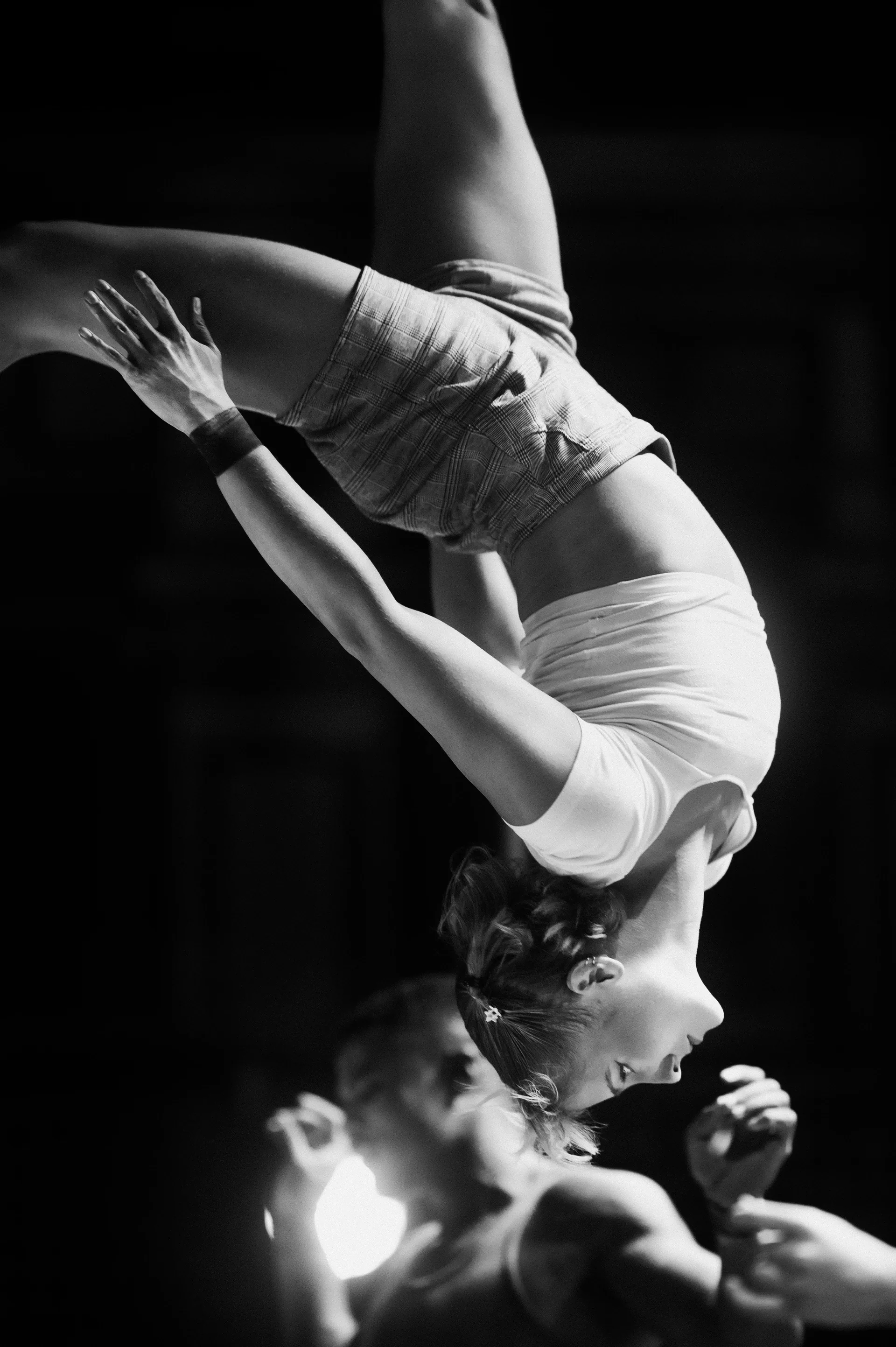 Acrobat curls upside down above a partner's raised feet.