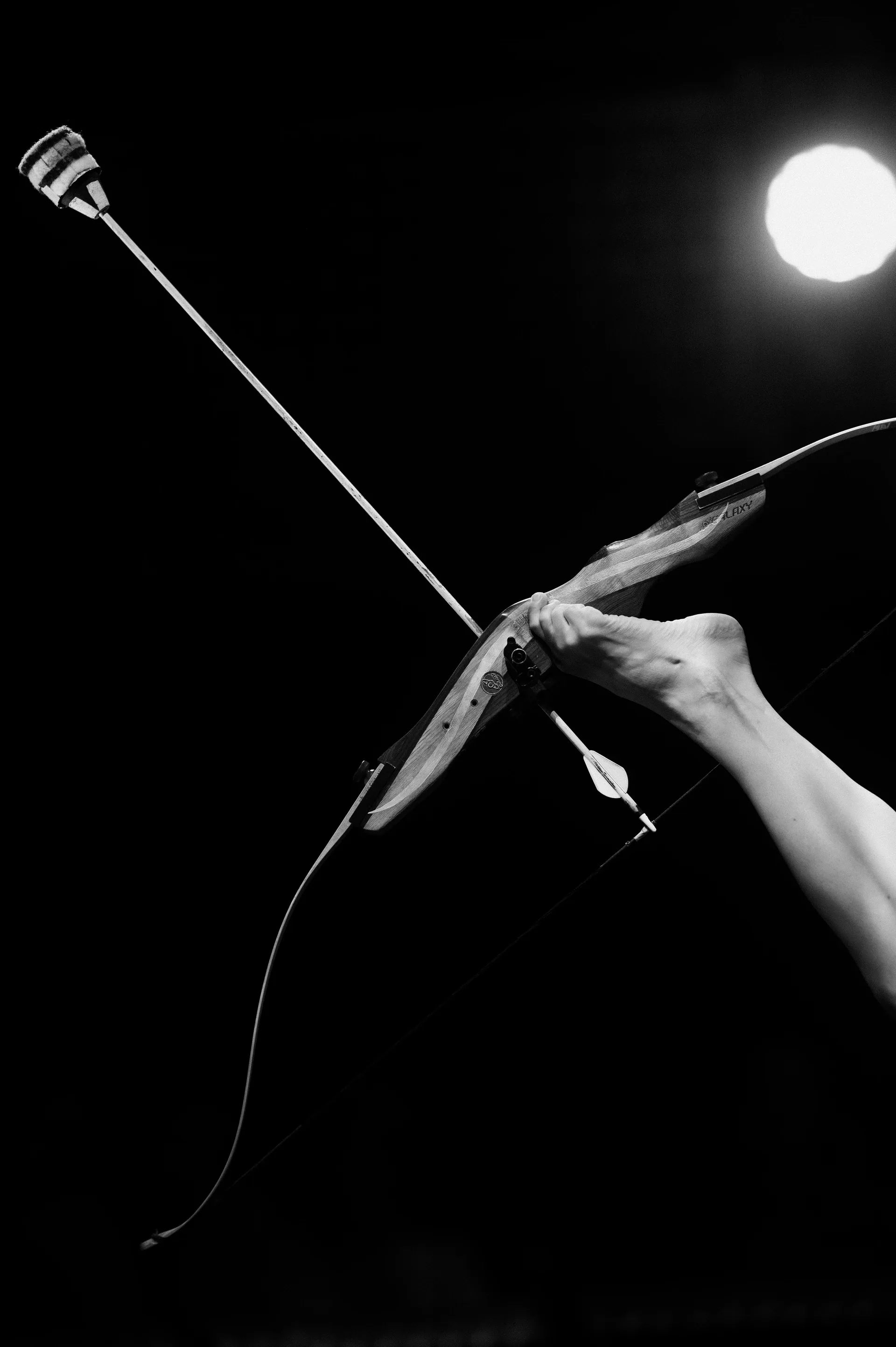 Bare feet hold a bow and arrow beneath a bright stage light.