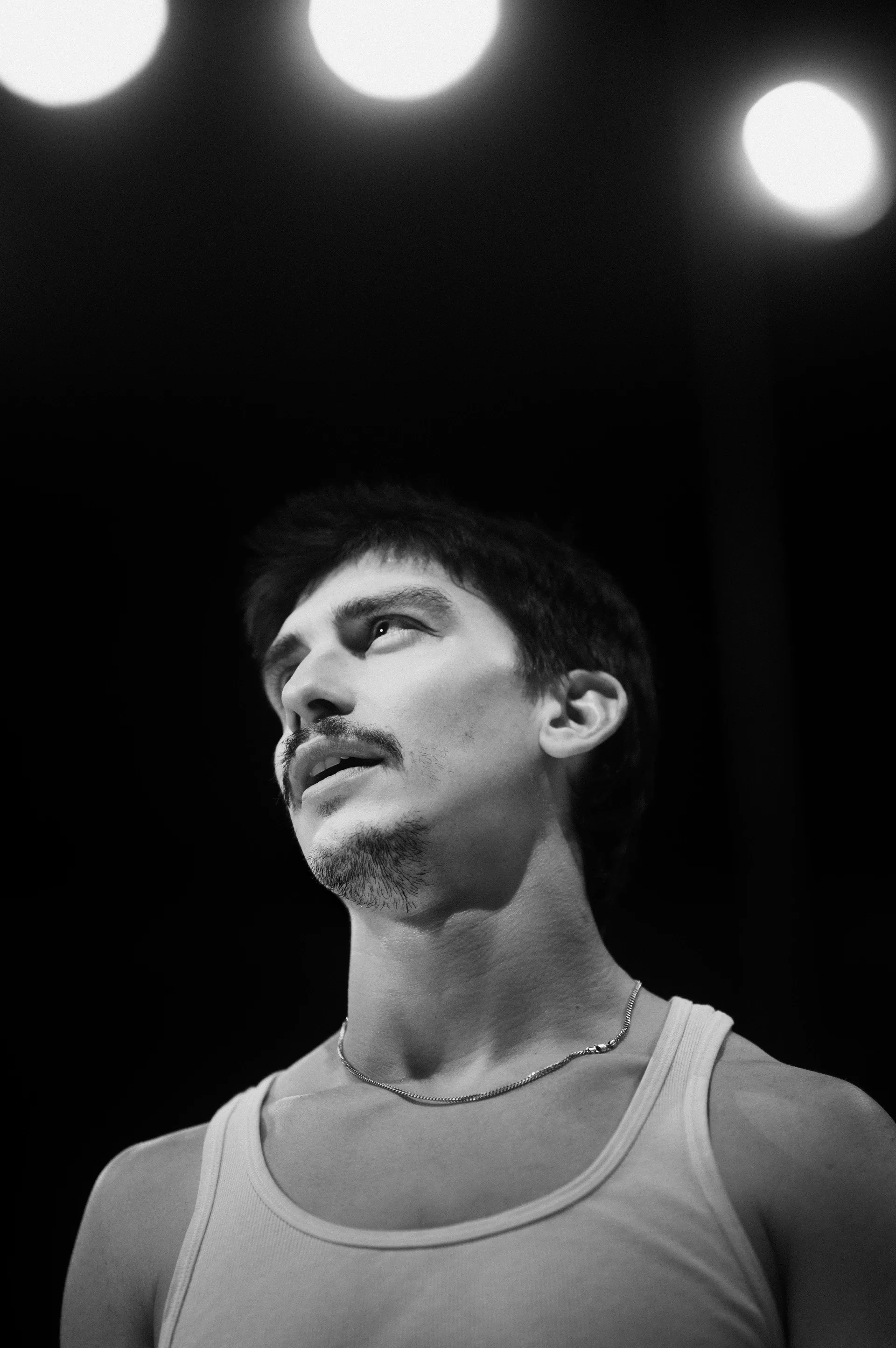 Performer looks upward beneath three stage lights.
