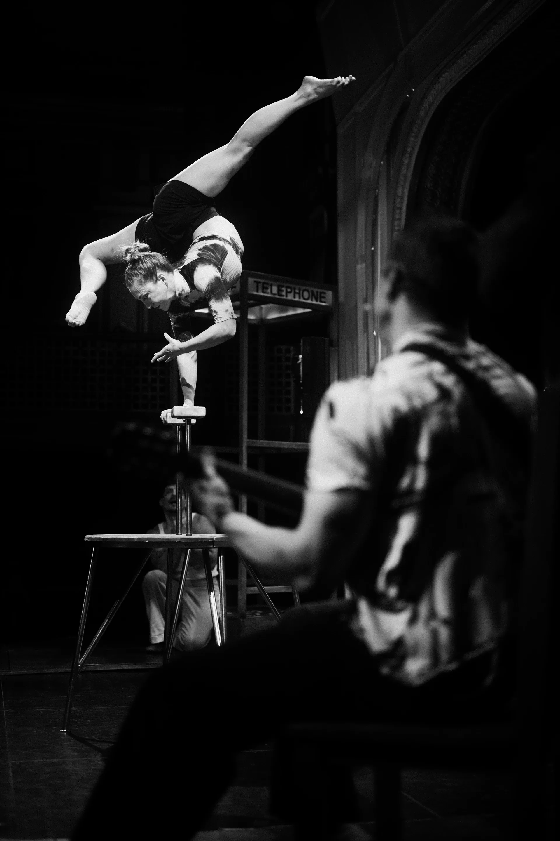 Acrobat holds an inverted balance on one arm atop a small platform.