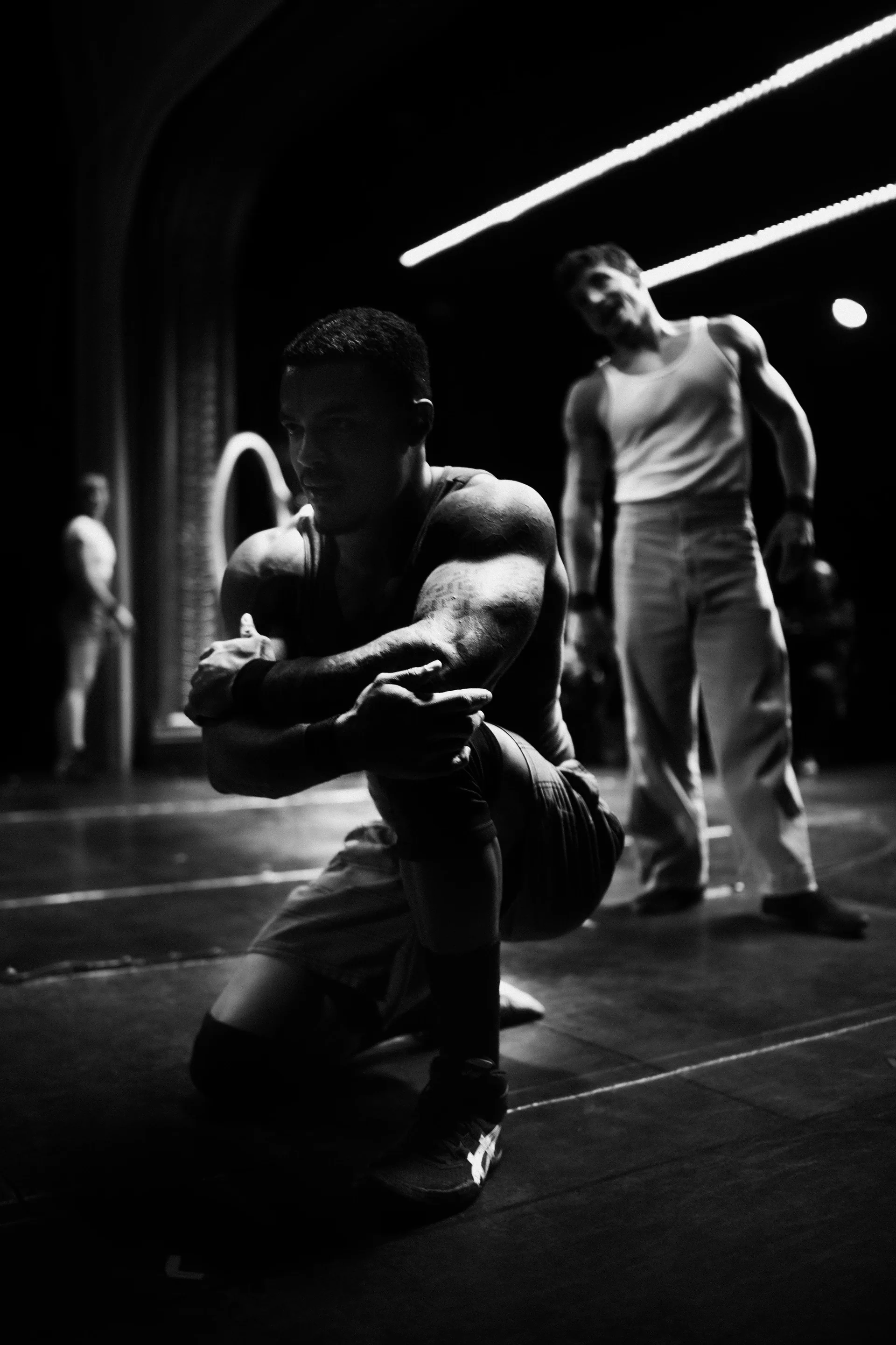 Kneeling performer holds both hands forward while another stands behind.