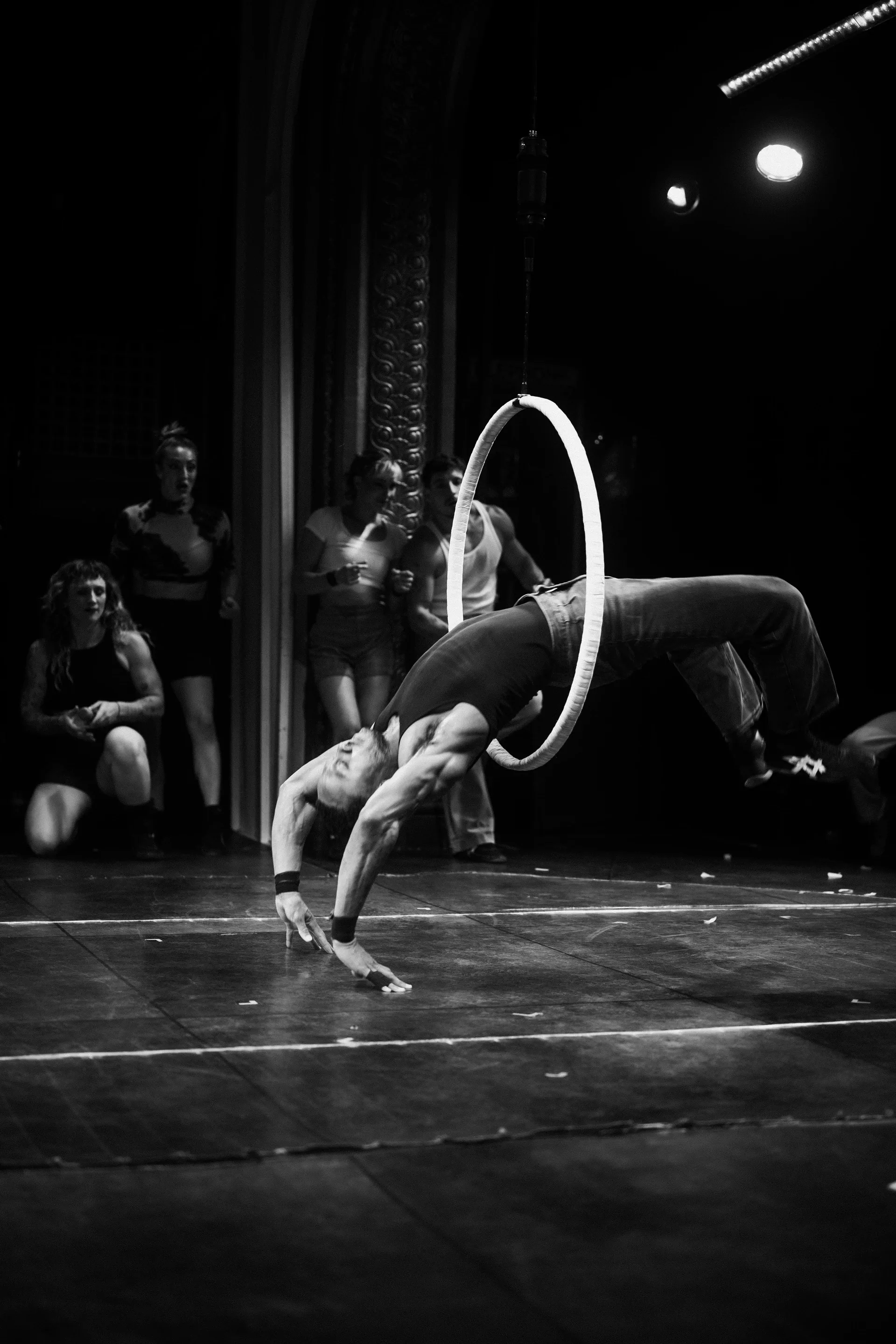 Acrobat bends backward through a large hoop with one hand on the floor.