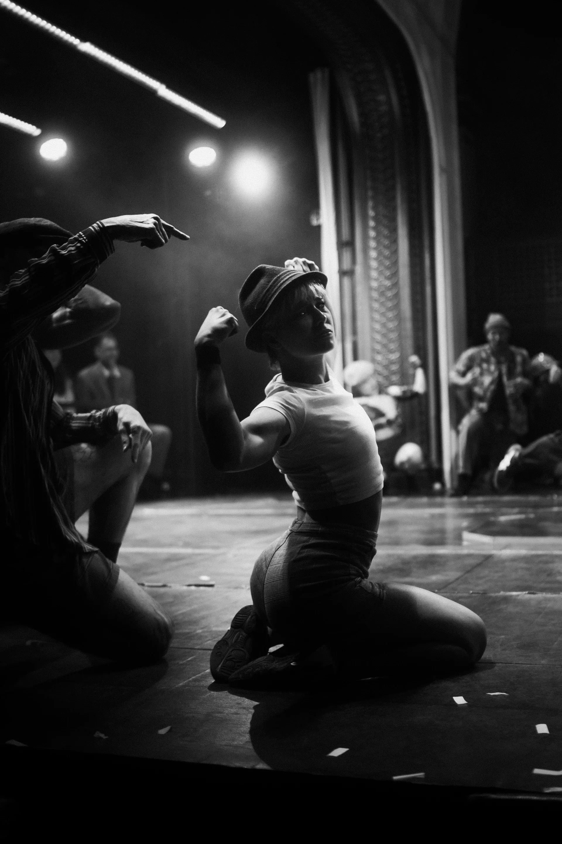 Performer sits on the stage with one hand raised toward the face.