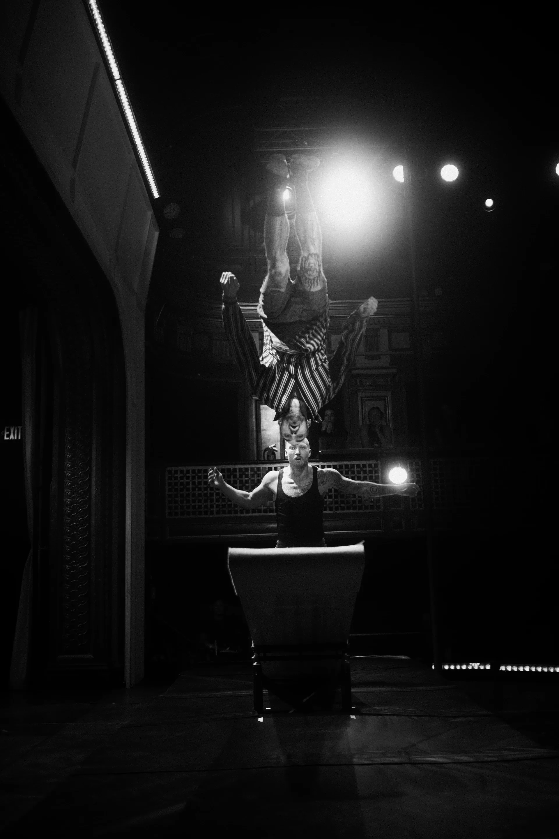 Performer holds an inverted balance on a raised apparatus beneath bright lights.