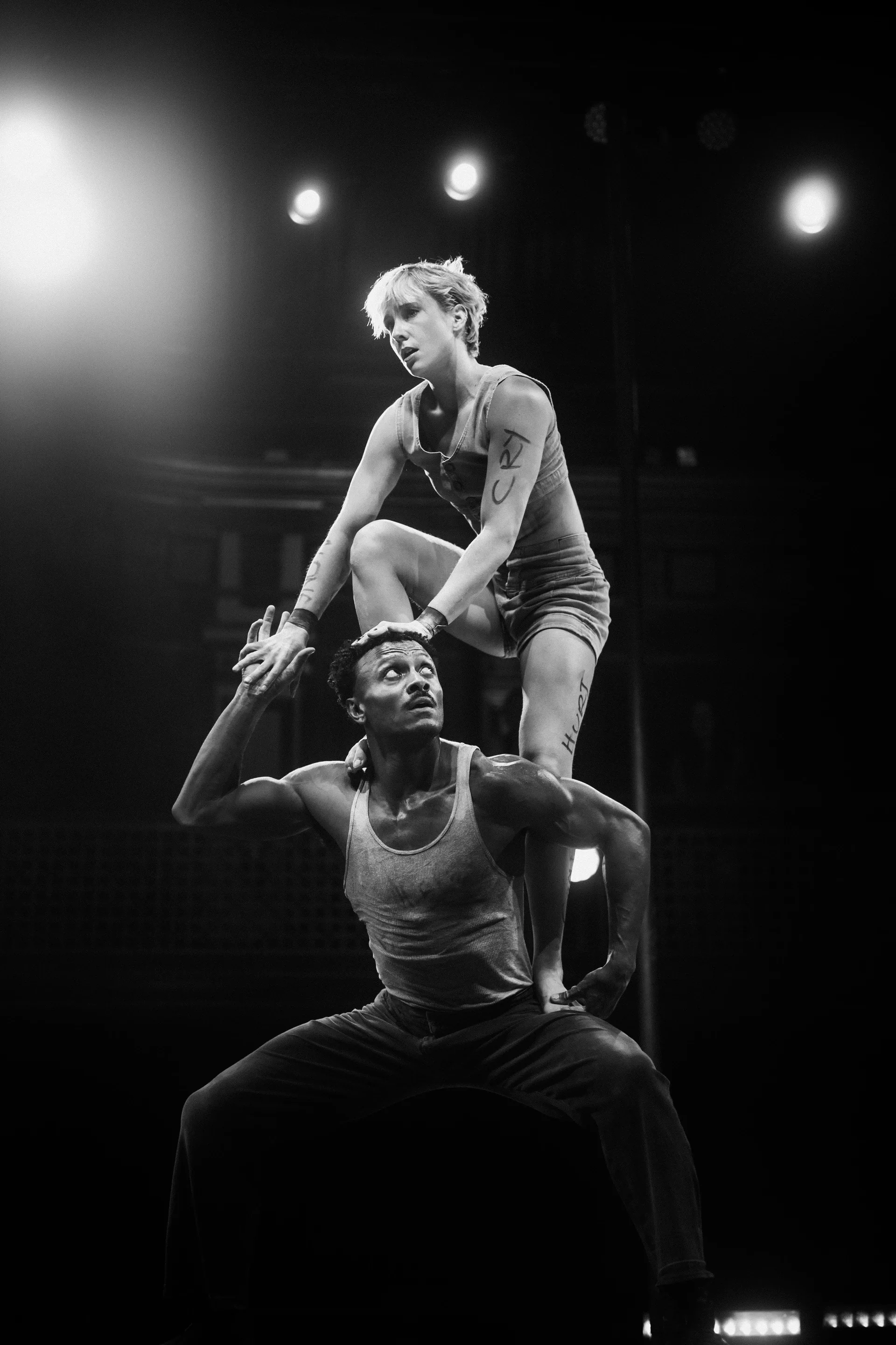 Performer balances on a partner's shoulders while both face forward.