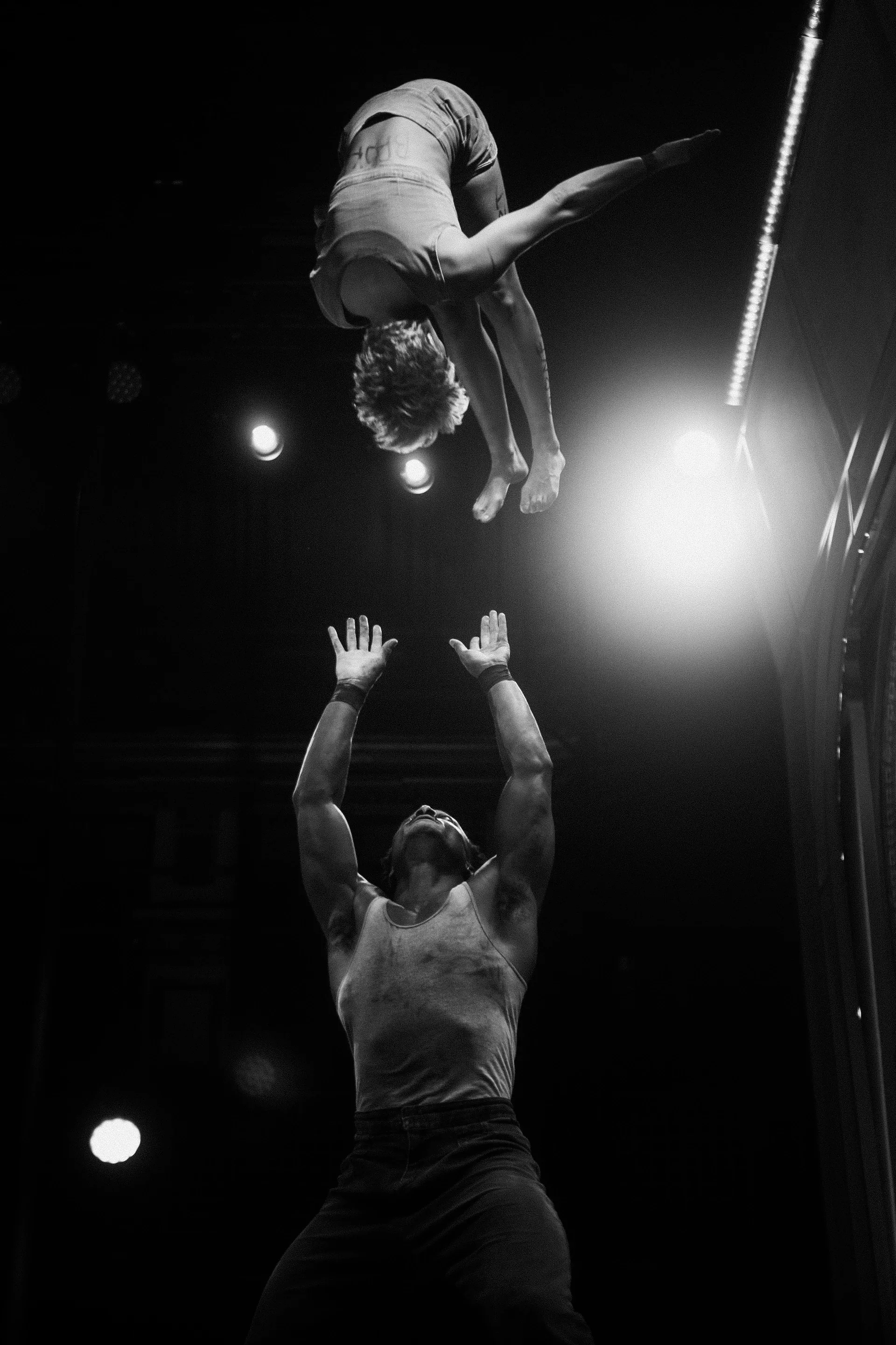 Acrobat is airborne above a partner's outstretched hands.