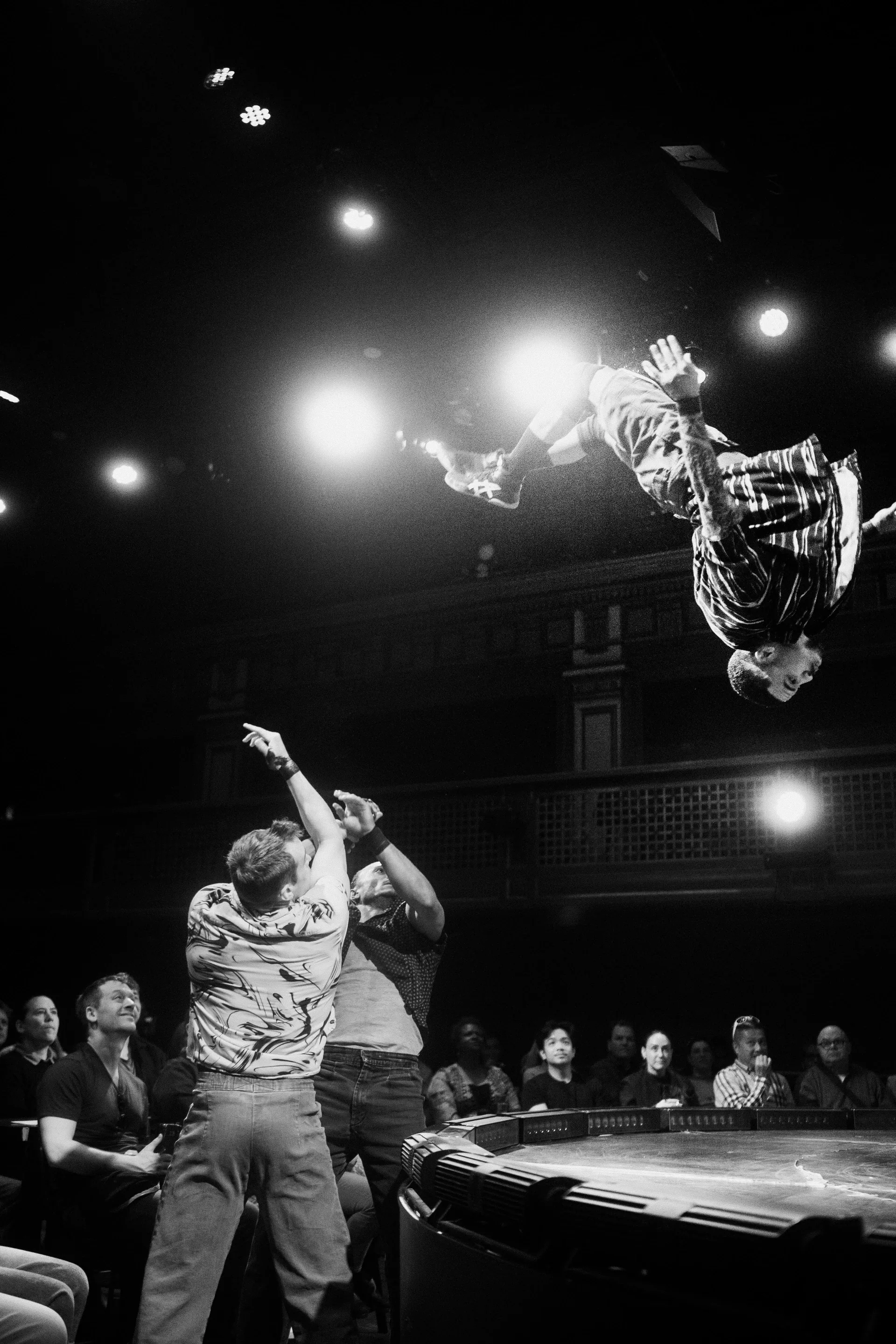 Acrobat flips over a partner at the edge of a circular stage.