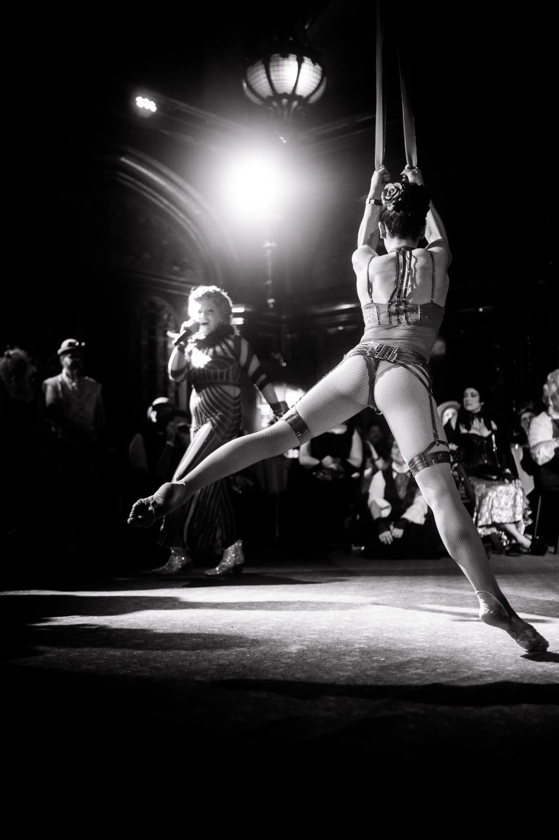 Aerialist hangs upside down from straps above the audience.