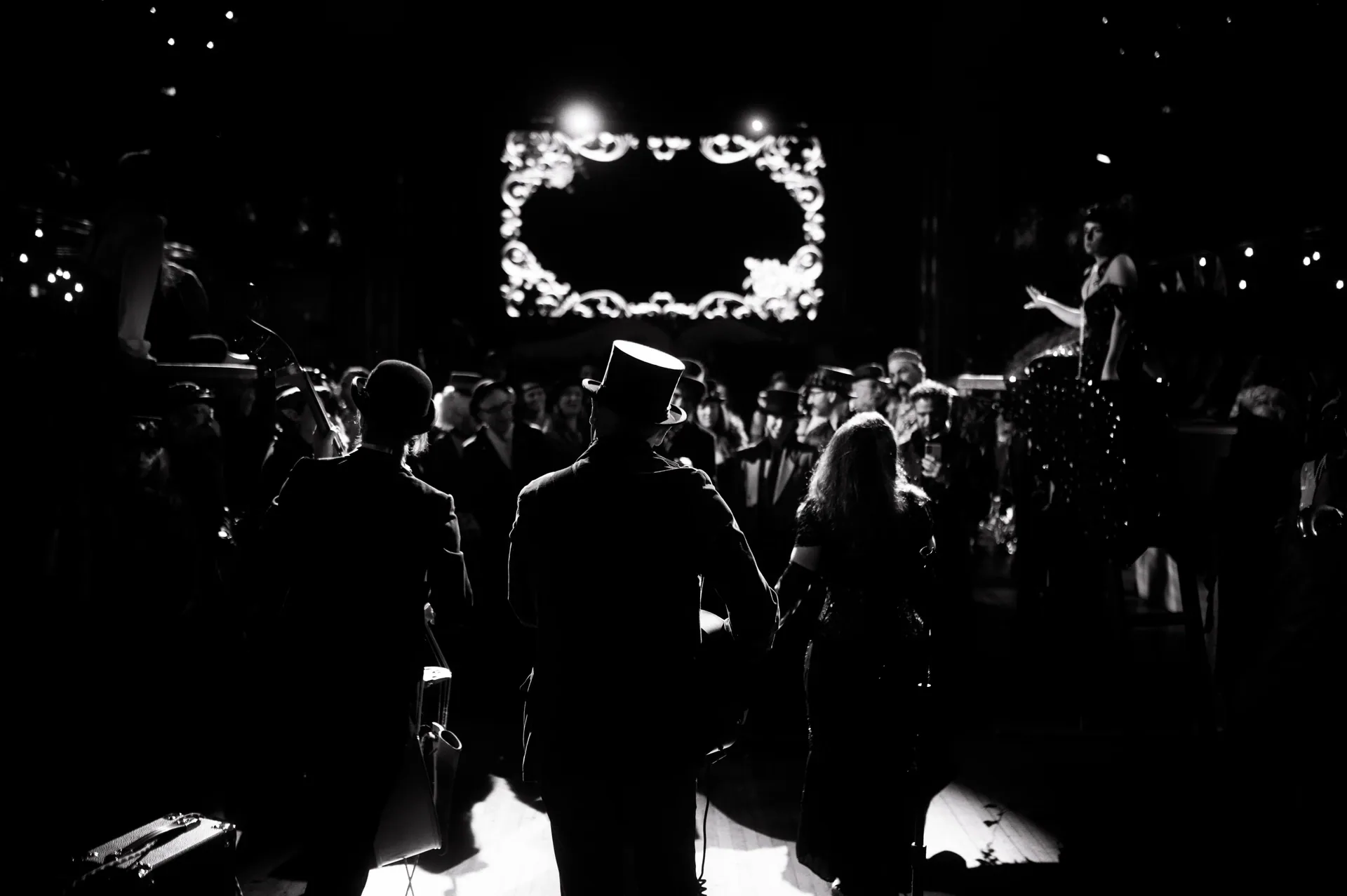 Crowd faces a stage framed by a bright decorative screen.