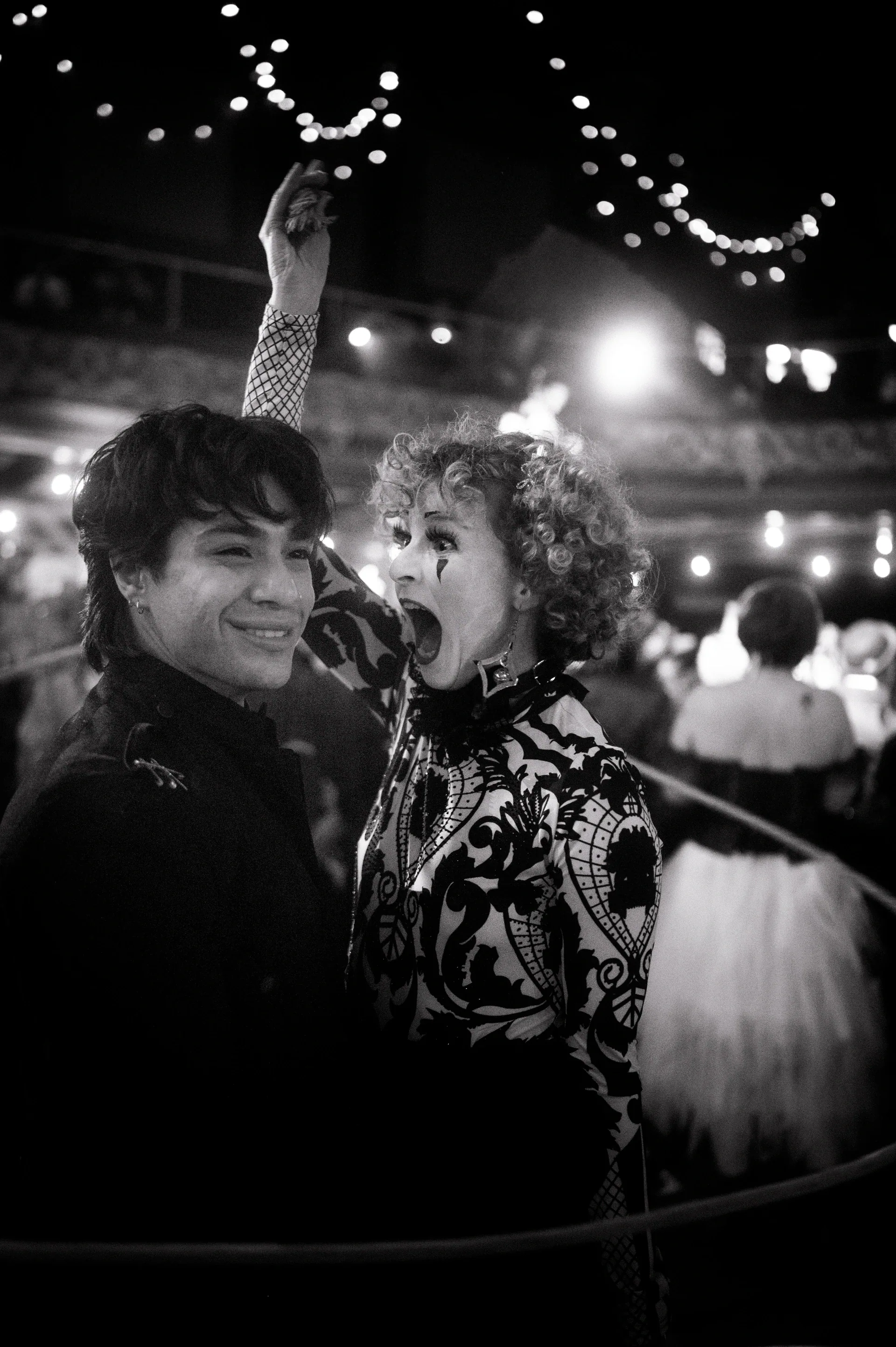 Two formally costumed attendees pose closely together beneath string lights.