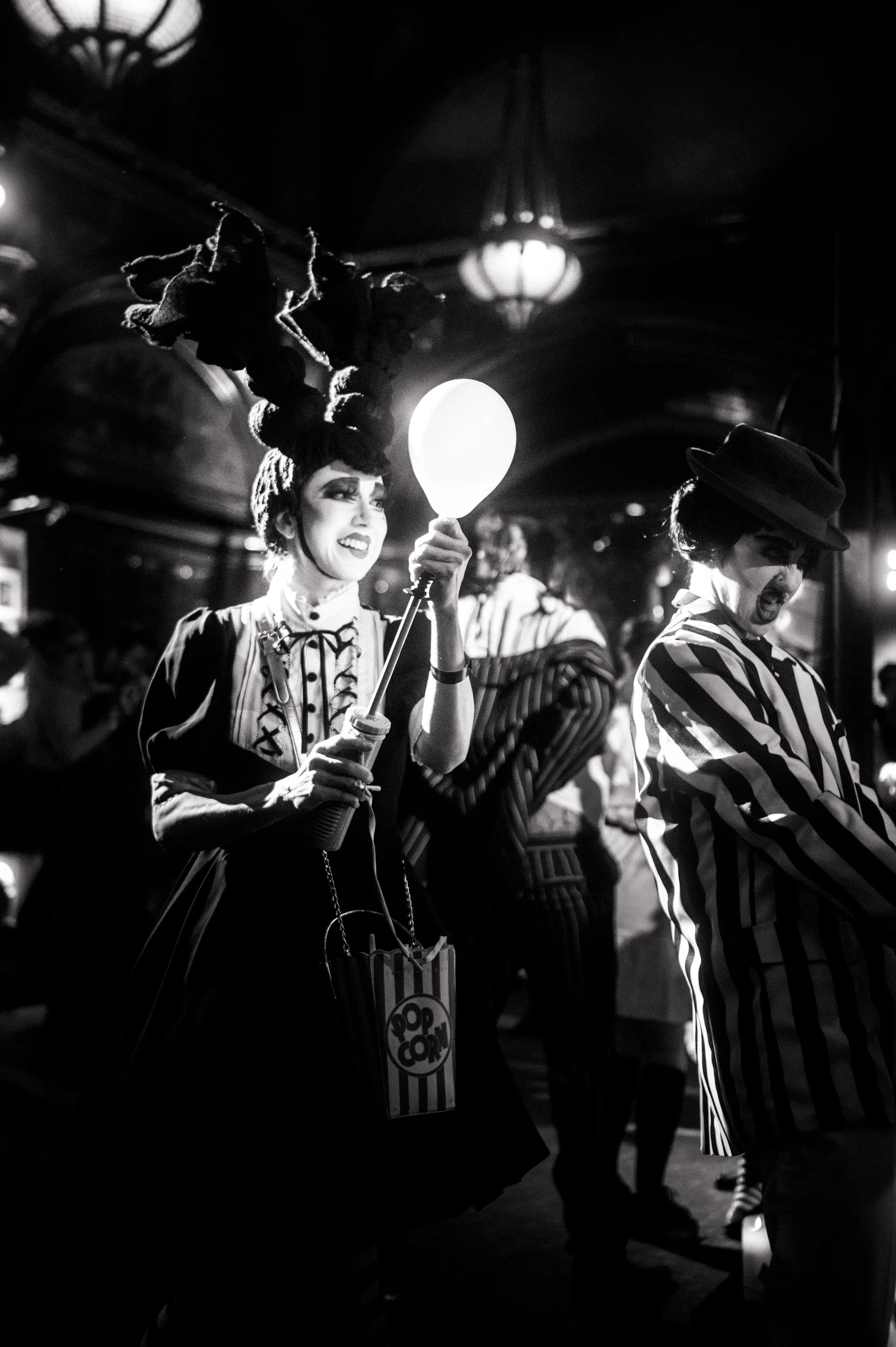 Two performers in striped costumes pose beside a large moon-shaped prop.